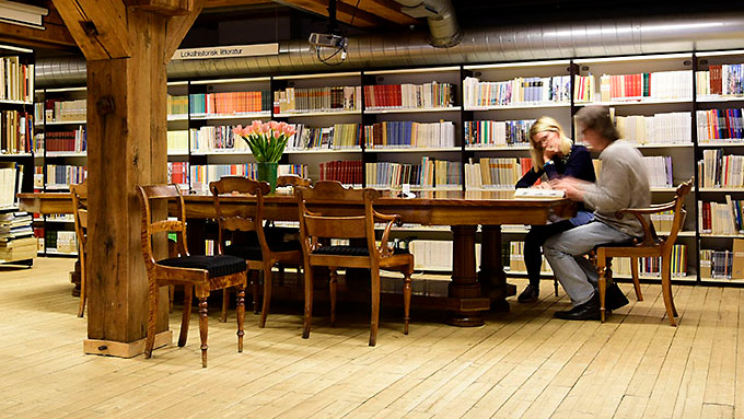 Mennesker som sitter og leser rundt et bord i biblioteket.