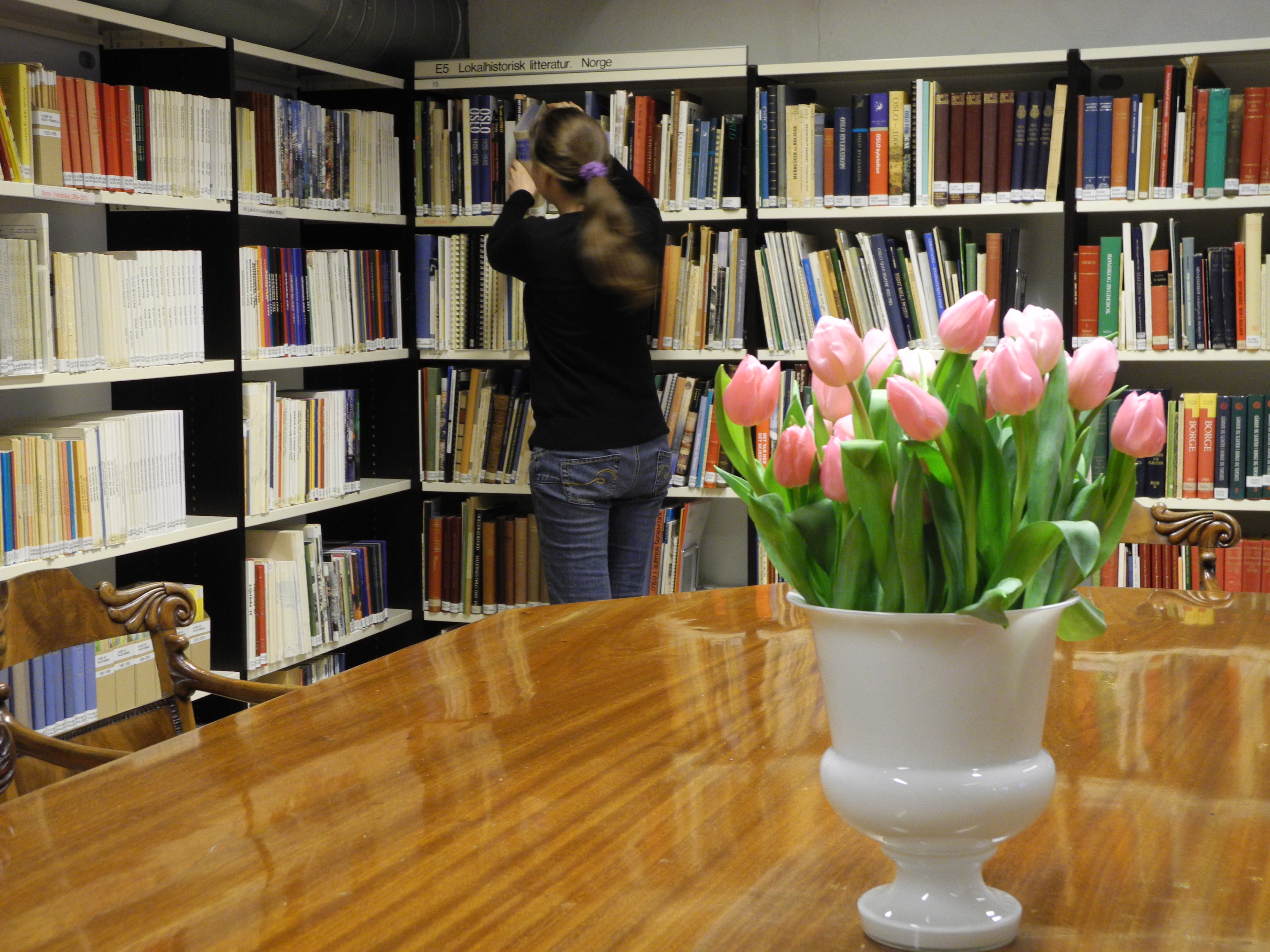 Bibliotekbruker henter ei bok fra hyllene