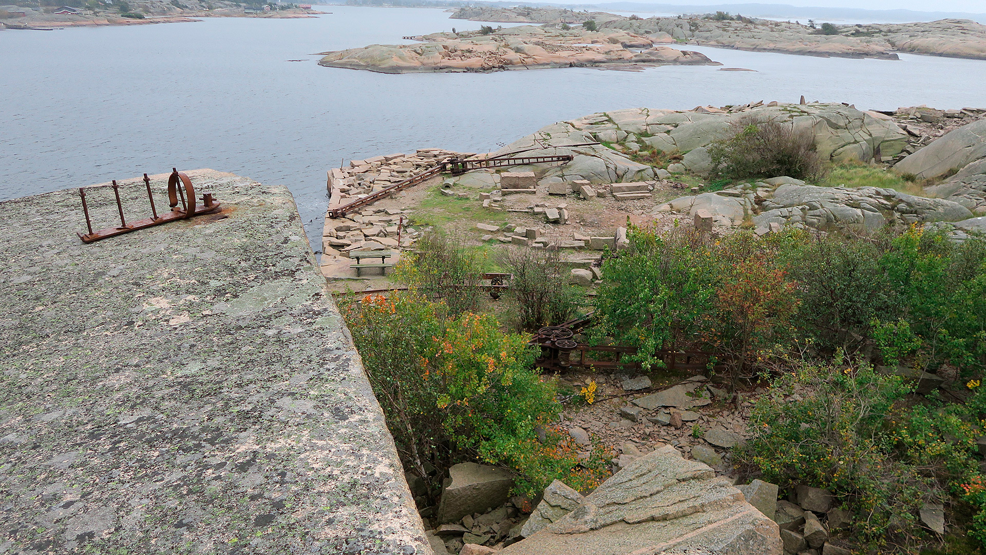 Foto av Utsikt over en del av området med granittblokker liggende i terrenget, og med en av kranene liggende på bakken. Fotografert av Ståle Arfeldt Bergås