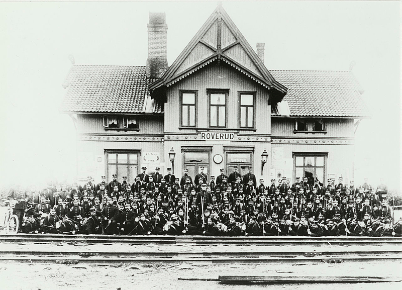 Foto av Roverud Jernbanestasjon med arbeidsstyrken foran. Fotgraf er Olga Kristoffersen, og bildet er hentet fra Riksantikvarens arkiv.