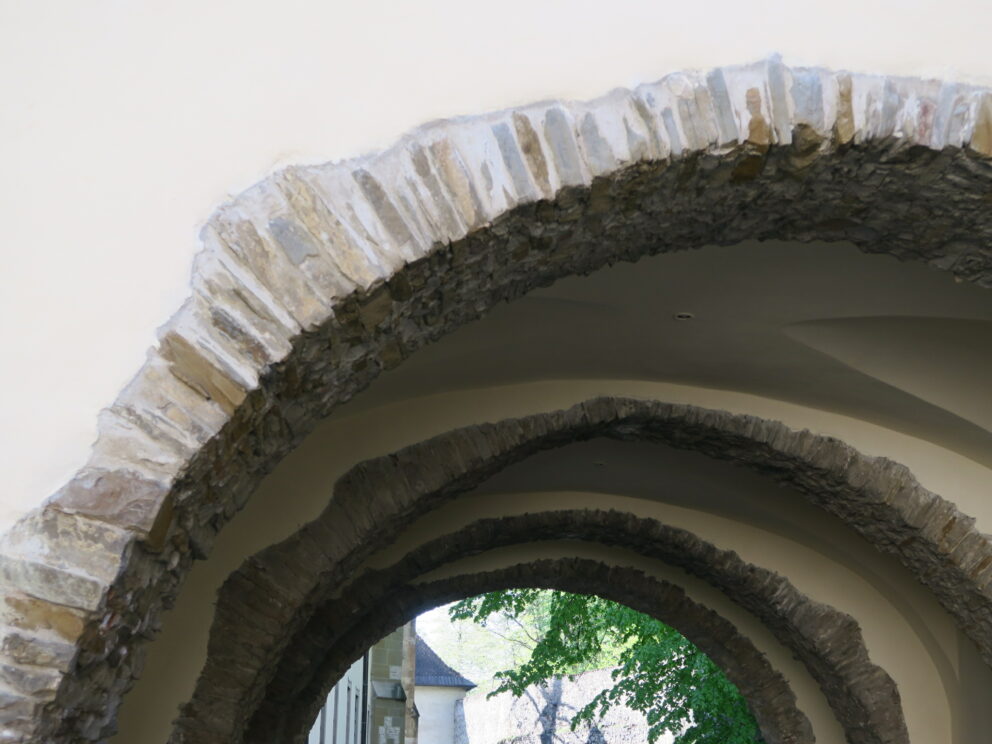 Steinbuer med grove kanter danner en tunnelaktig passasje, med sollys og grøntområder synlig gjennom åpningen i den andre enden.