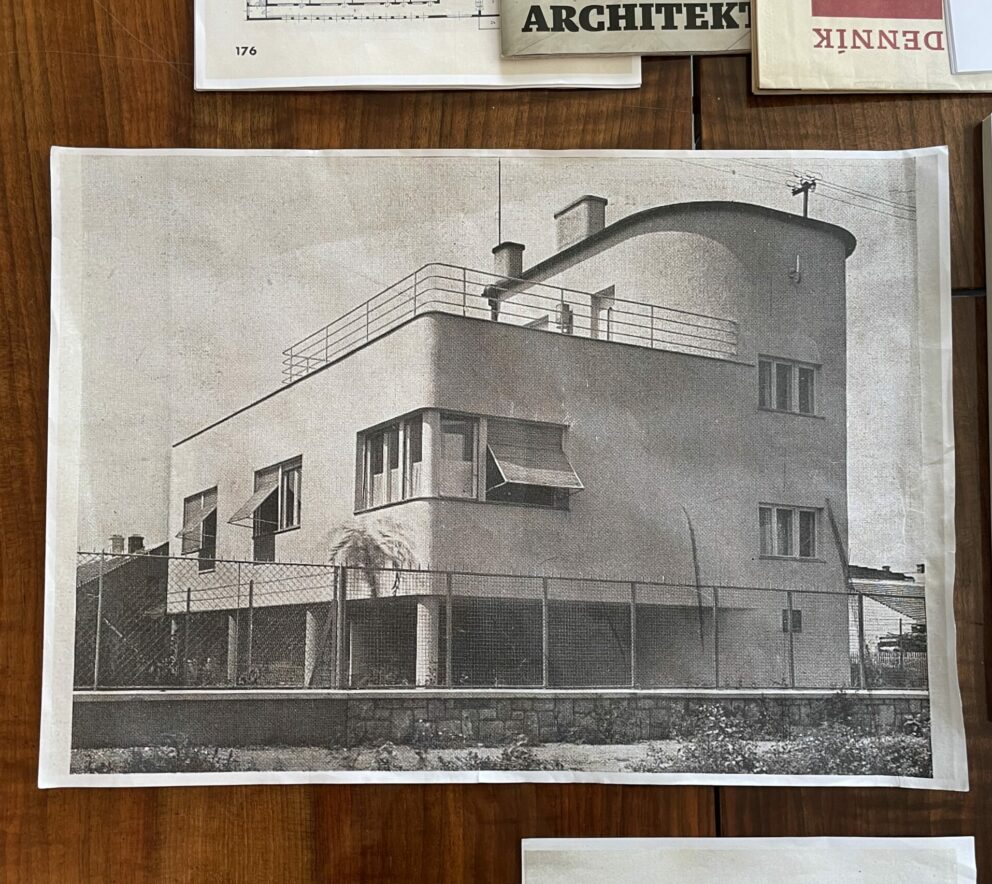 En samling foto og avisutklipp på et bord. Et stort bilde av en funksjonalistisk villa er sentralt.