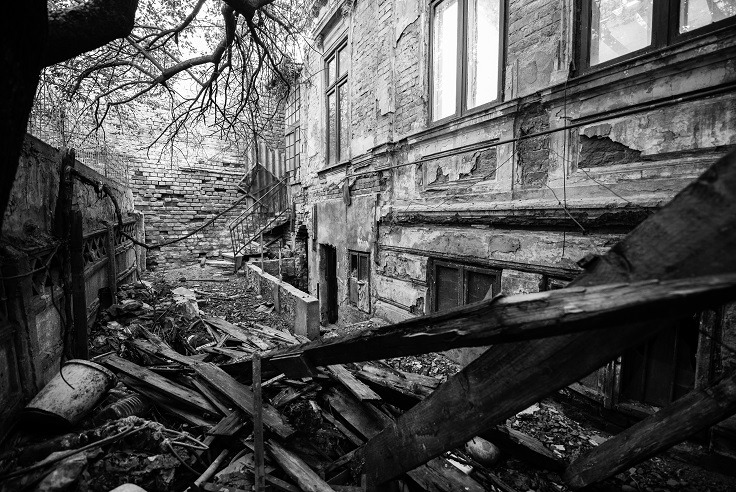 Sort/hvitt-bilde av en haug med planker, murstein og en delvis ødelagt trapp foran en forfallen bygning.