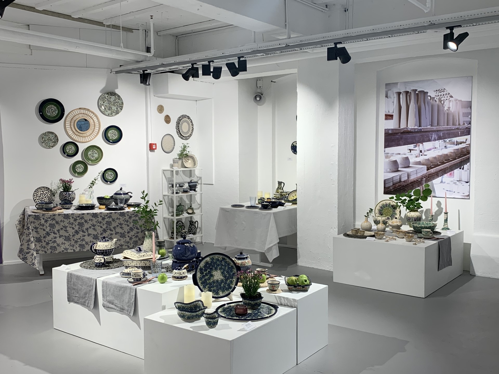 Et hvitt utstillingslokale hvor det er stilt ut fargerike keramikkgjenstander i blått, grønt og hvitt.
