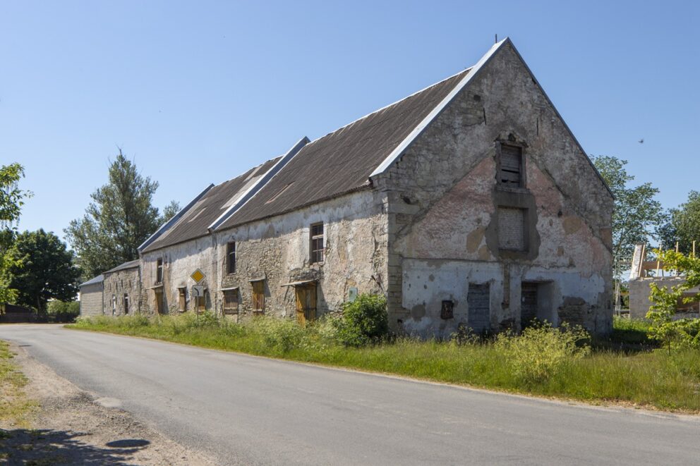 En slitt mursteinsbygning i to etasjer, med gjenspikrede vinduer og en slitt, gul dør, vei og grønt gress foran.
