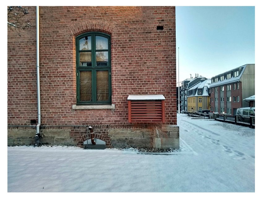 Varmepumpe gir god energibruk. En rødmalt varmepumpe på murveggen i Hamar fengsel.