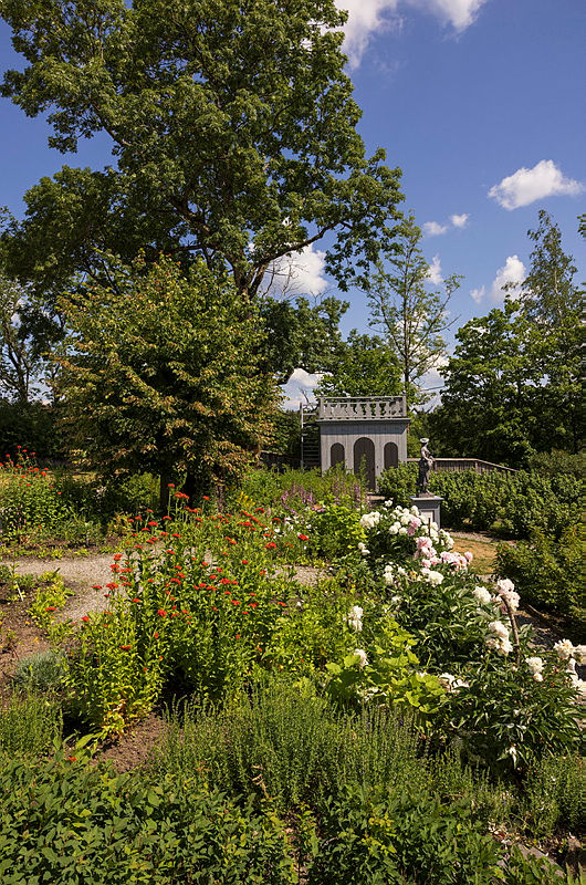Hagen på Spydeberg prestegård ved midtsommer, med frodige blomsterbed og utsiktspaviljong