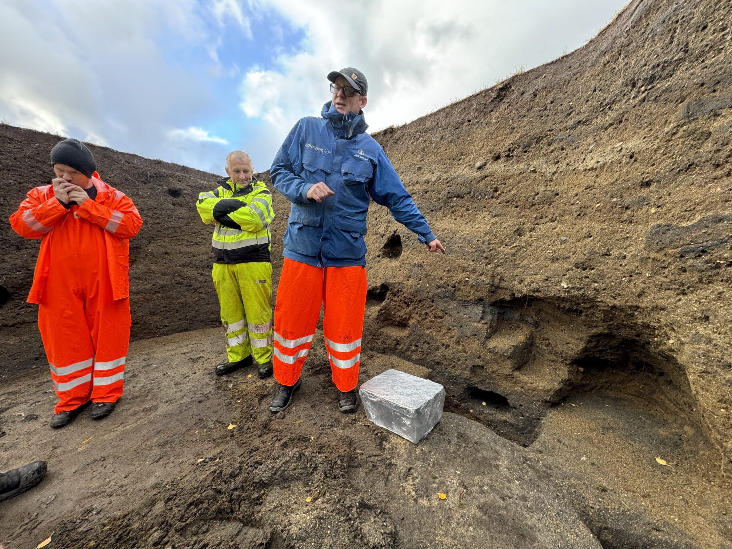 Bilde som viser UiB-arkeolog Morten Ramstad, mens han peker på hvor tidskapselen skal settes ned i gravhaugen på Myklebust i Nordfjordeid.