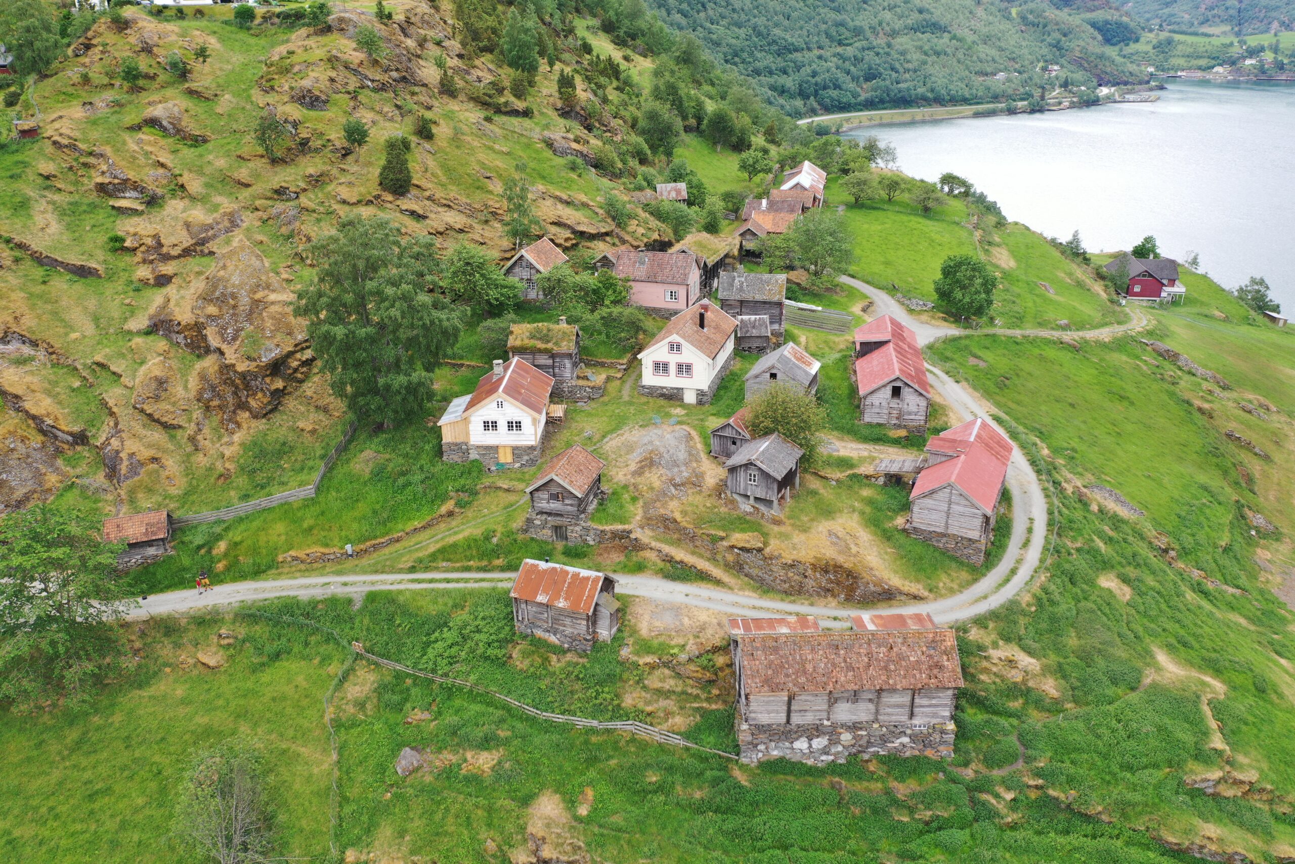Luftfoto av Otternes-tunet med trehus og låver spredt på grønne åser nær et vann.