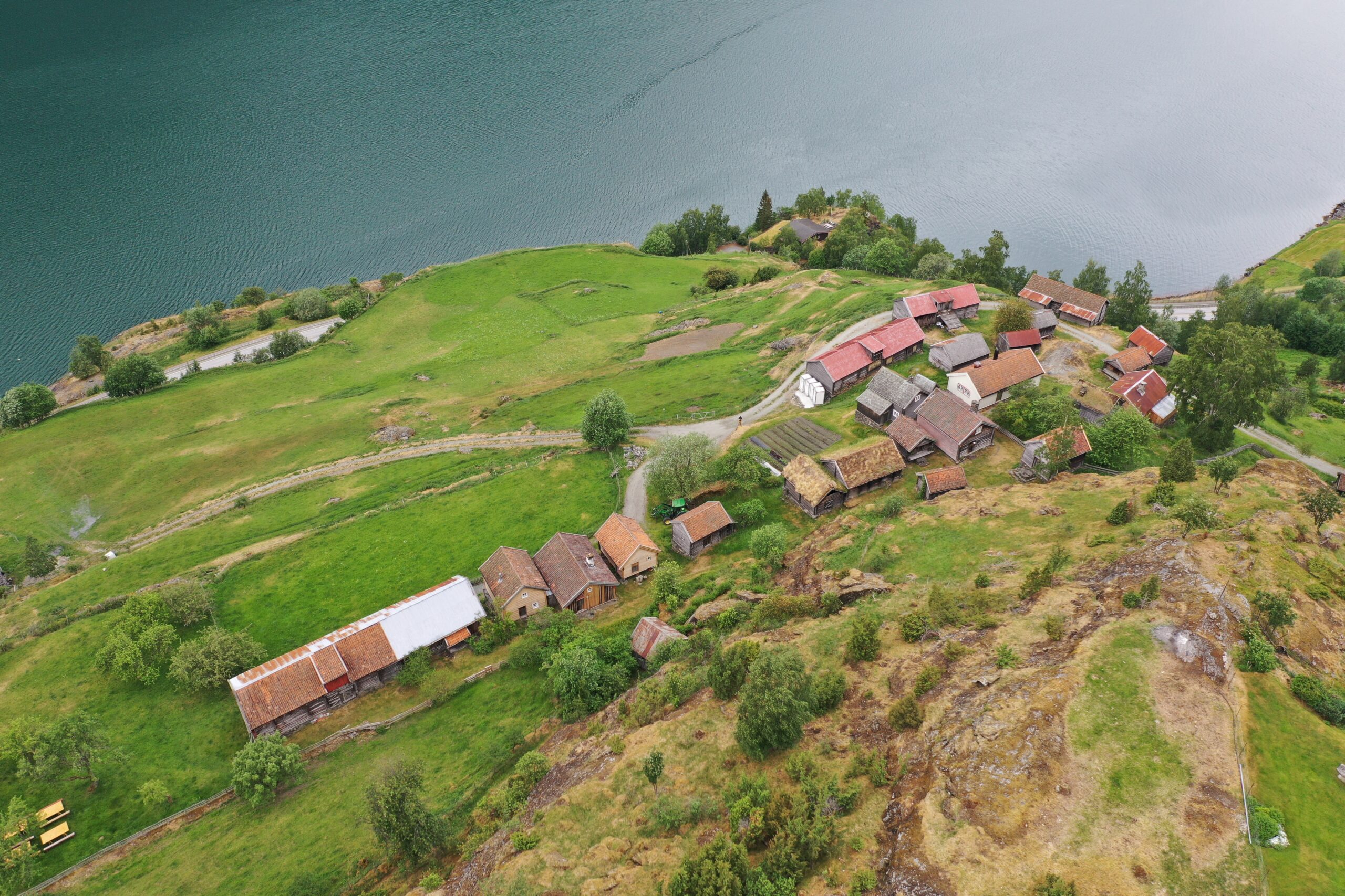 Luftfoto av Otternes-tunet med spredte hus og grønne jorder ved siden av et vann.