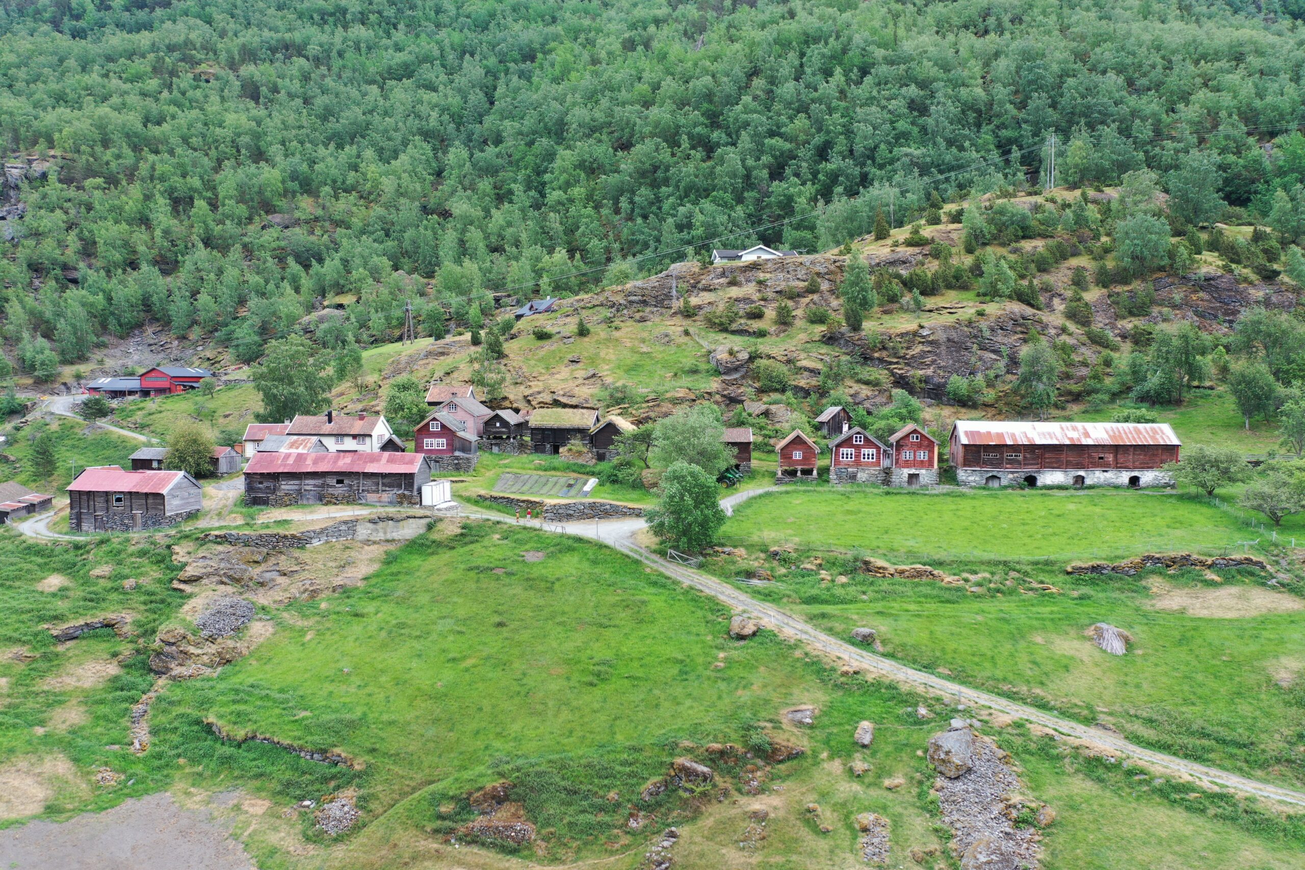 En liten klynge på Otternes-tunet med rustikke trebygninger med røde tak ligger i en grønn åsside omgitt av tett skog og gressletter.