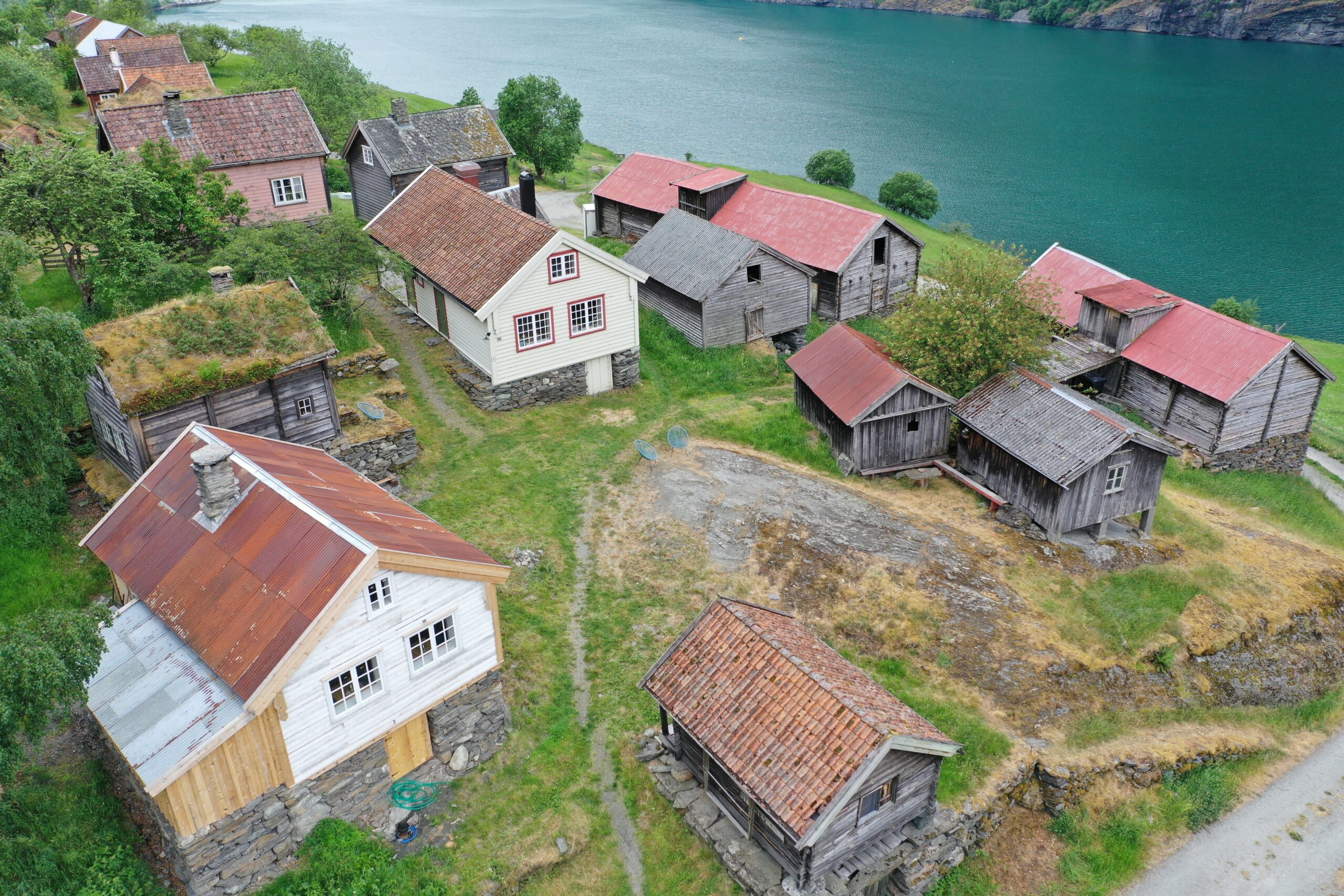 Luftfoto av Otternes-tunet med tradisjonelle trehus, noen med gresstak, som ligger i en åsside ved et vann.
