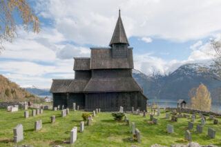 Bilde av Urnes stavkirke med fjord og fjell i bakgrunnen.