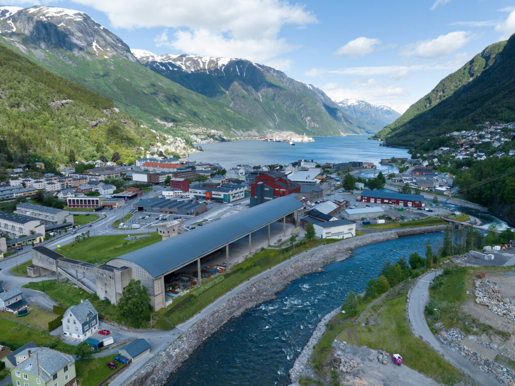 Luftfoto som viser Odda og Odda smelteverk - med fjellene og fjorden i bakgrunnen.