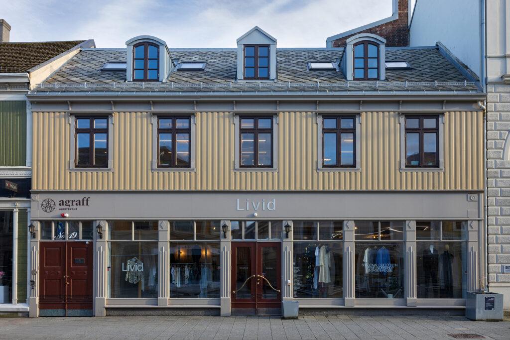 En toetasjes bygning med beige ytterkledning og tre kvistevinduer på taket; i første etasje er det store glassvinduer og skilt for Livid og agraff.