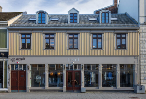 En toetasjes bygning med beige ytterkledning og tre kvistevinduer på taket; i første etasje er det store glassvinduer og skilt for Livid og agraff.