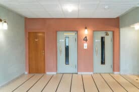 To lysegrønne heisdører og en tredør er plassert i en rosa vegg merket 4 i en godt opplyst, ryddig oppgang med stripete gulv.