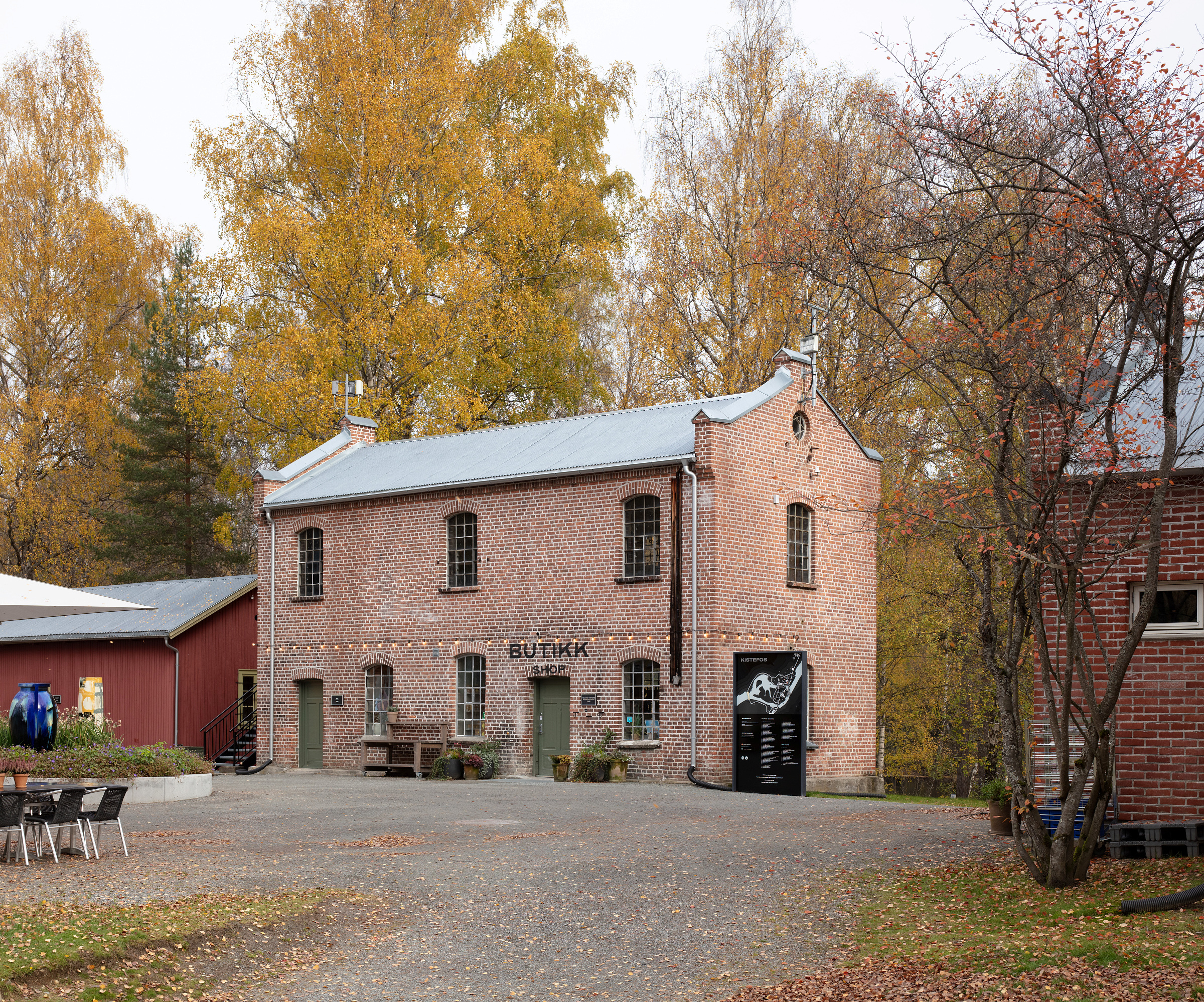 En toetasjes murbygning med skiltet BUTIKK er omgitt av høsttrær ved smia og verkstedet på Kistefos Træsliberi