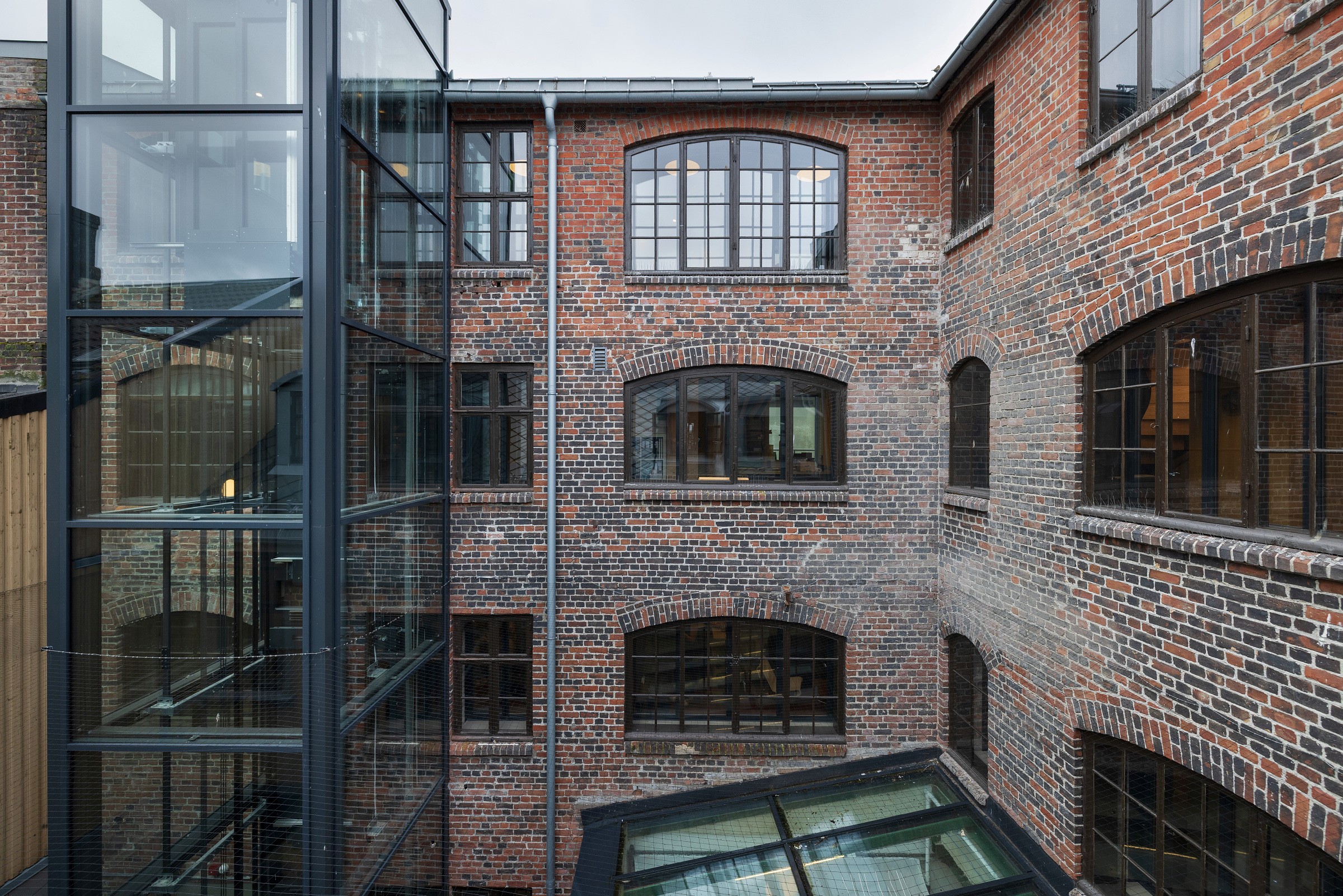 En industribygning i murstein med store buede vinduer og en moderne heissjakt i glass på gårdsplassen.