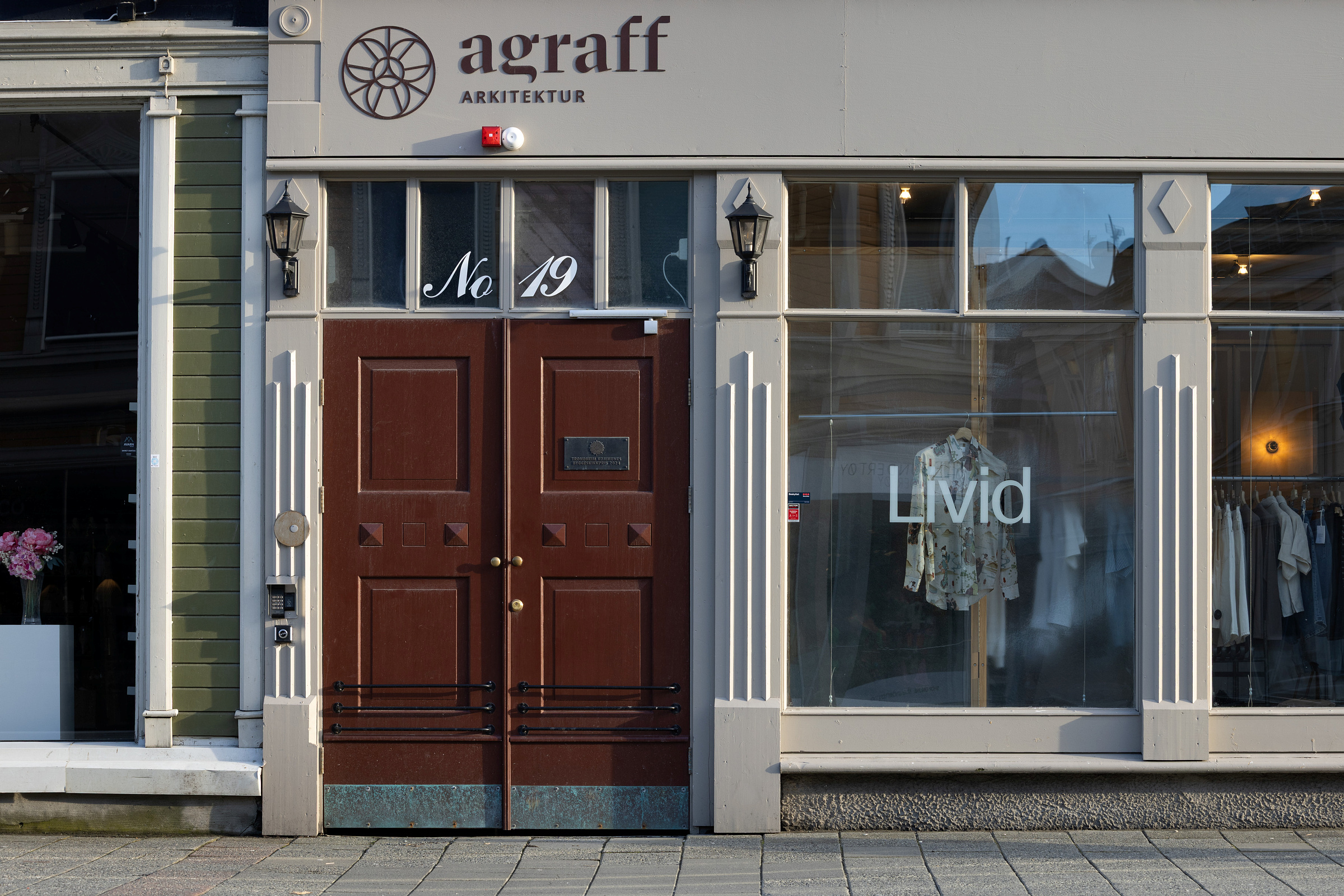 Butikkfasade med brune dobbeltdører merket nr. 19, med agraff ARKITEKTUR over, og et stort vindu med klær og ordet Livid.