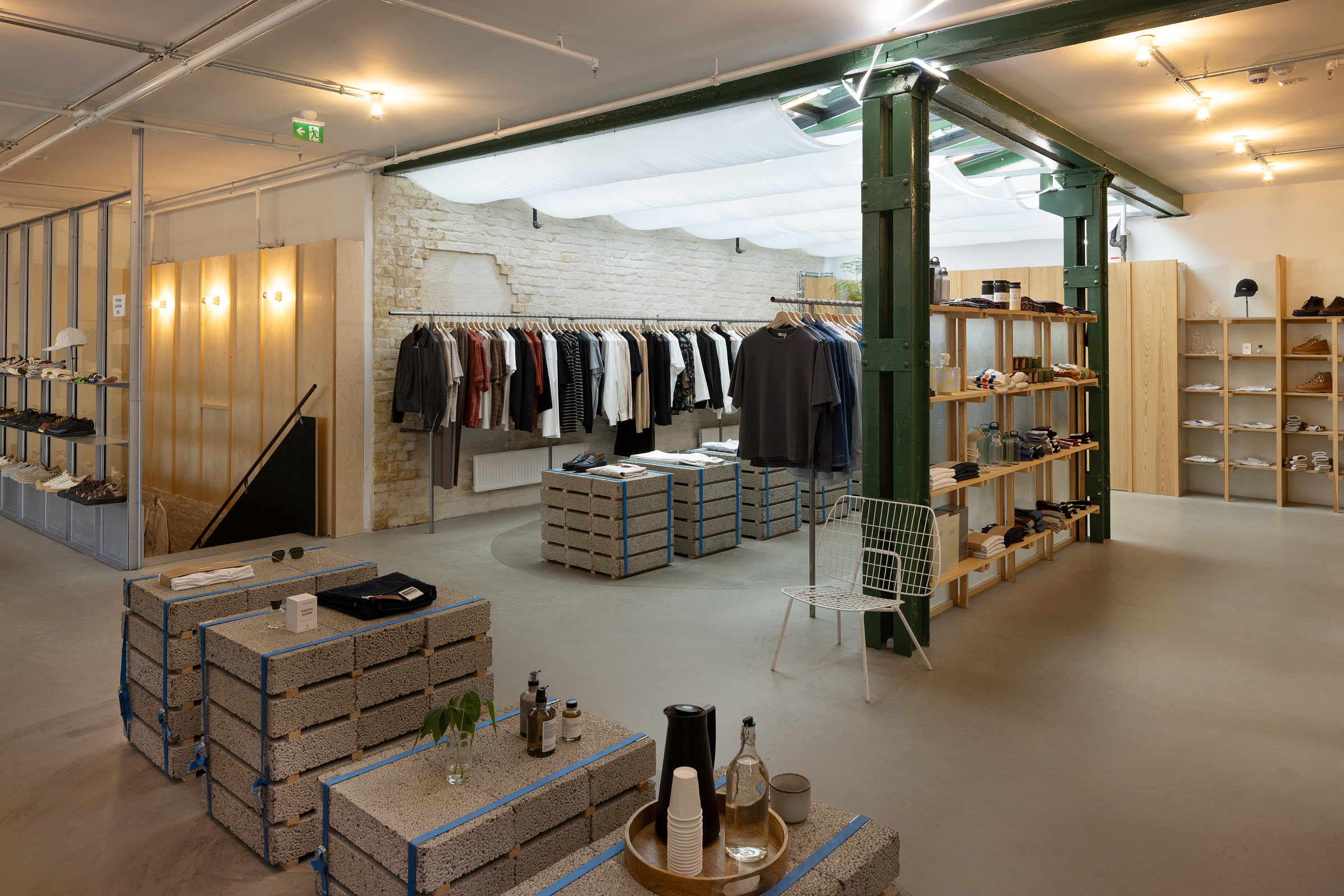 En moderne klesbutikk med eksponerte murvegger, hengende plagg, hyller med sko og tilbehør og møbler laget av betongblokker.