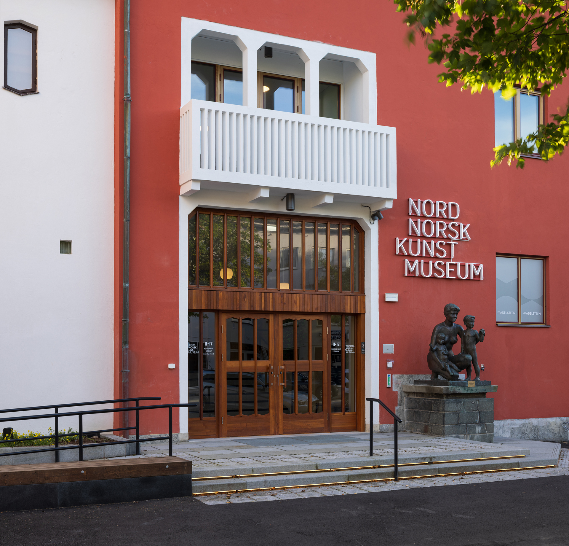Hovedinngangen til Nordnorsk Kunstmuseum med en stor tredør, hvit balkong over og en bronsestatue på en steinsokkel utenfor.
