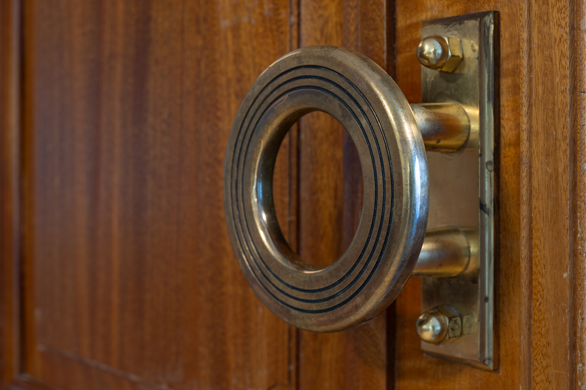 Nærbilde av et stort, rundt dørhåndtak i messing montert på en tredør med vertikale paneler.