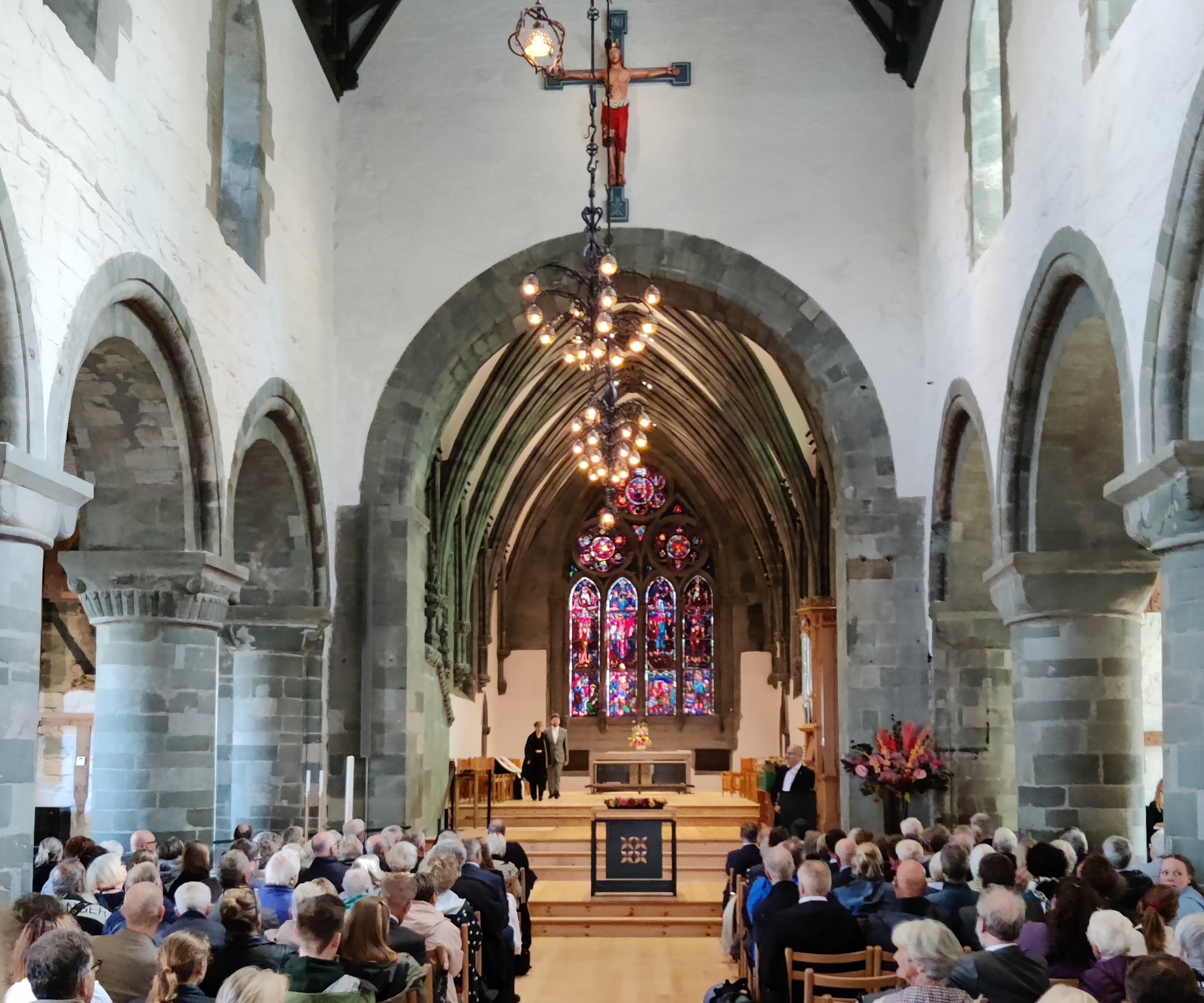 En forsamling sitter inne i Stavanger domkirke, med hvelvede tak, glassmalerier bak alteret og et stort krusifiks som henger fra taket.