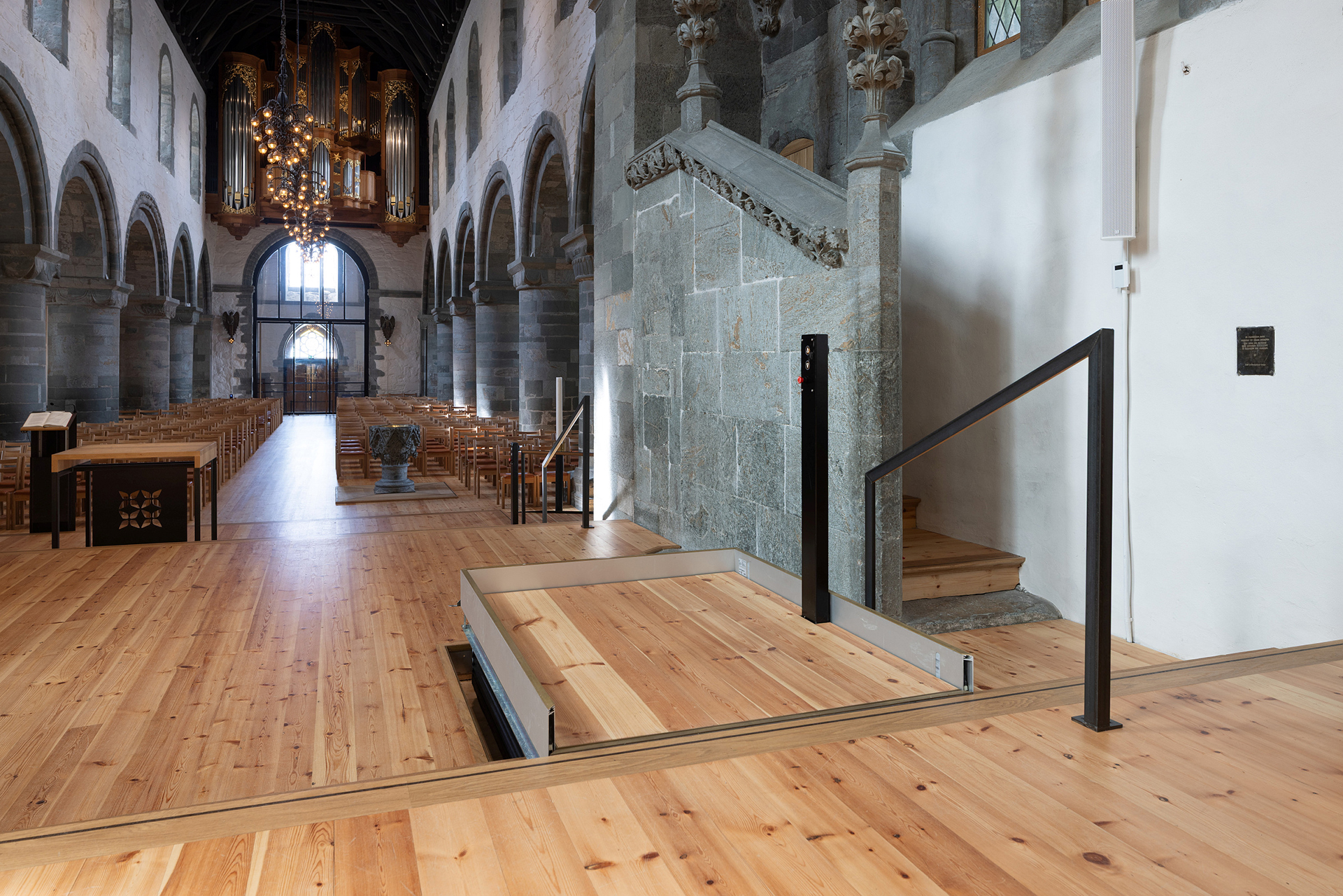 Moderne tilgjengelegheit i mellomalderkyrkje 14 En rullestolheis er installert ved siden av en steintrapp inne i en historisk kirke med tregulv, buede søyler og stolrader.