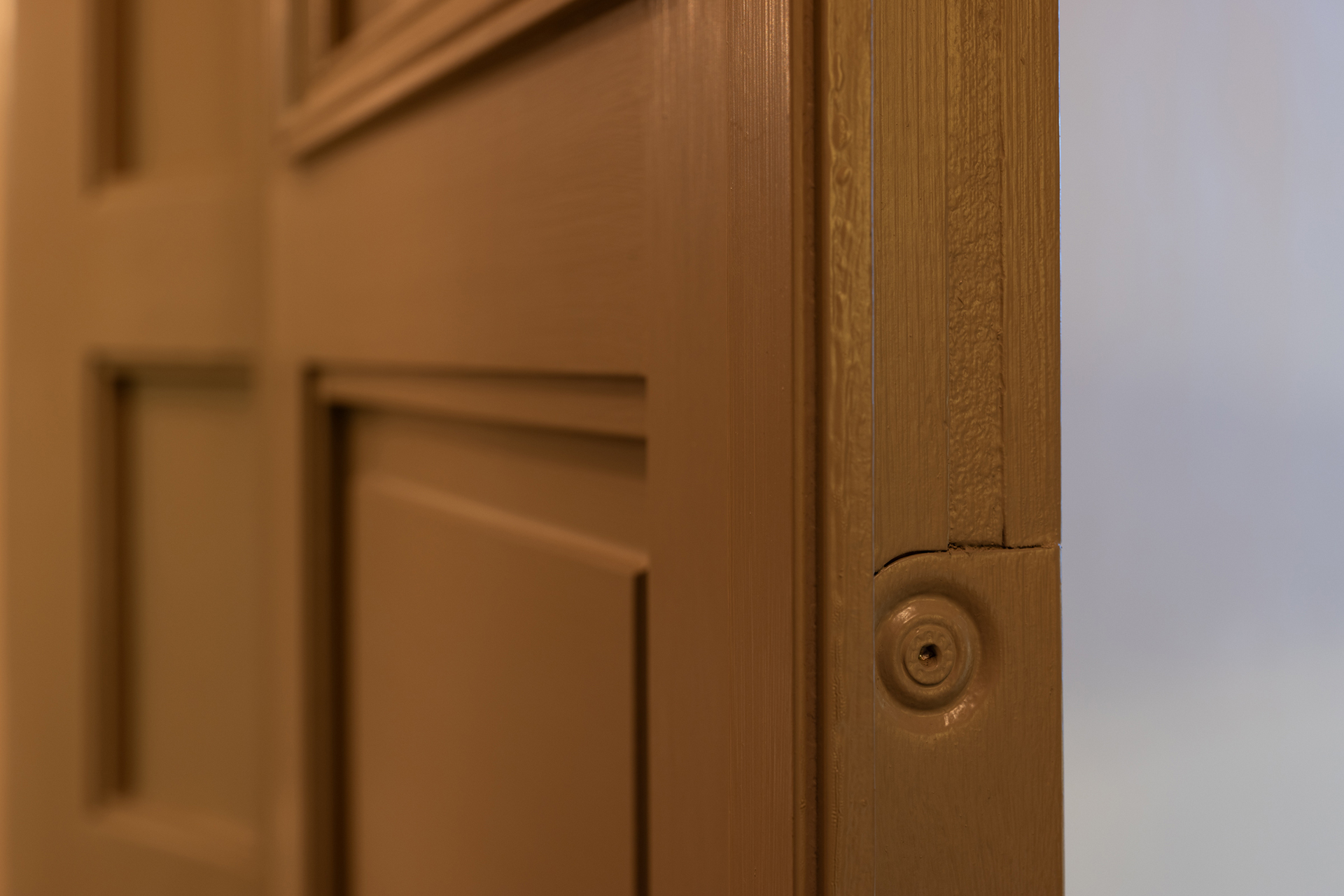 Nærbilde av en delvis åpen, brun tredør, med fokus på kanten og dørkarmen, uten synlig håndtak eller lås.
