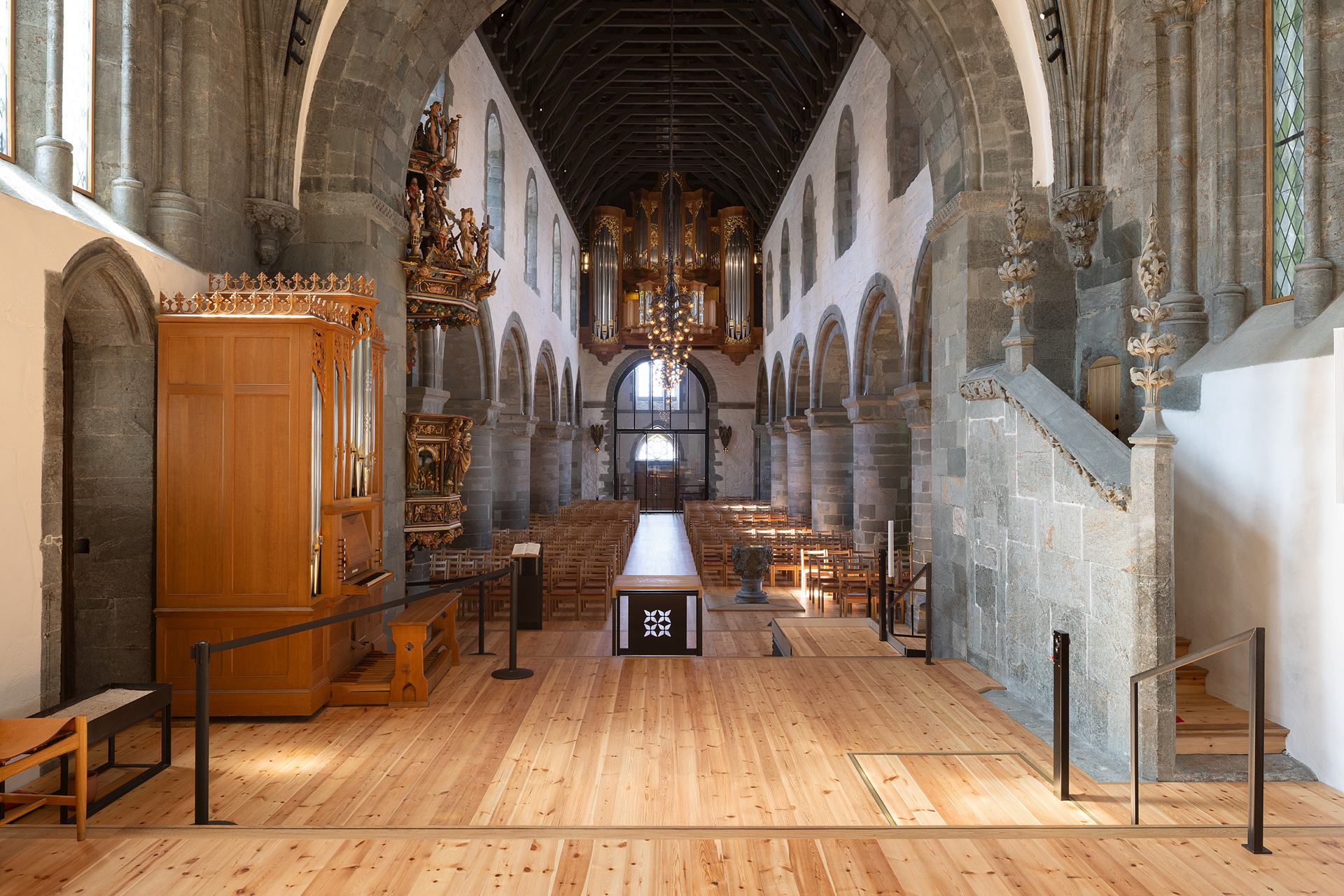 Moderne tilgjengelegheit i mellomalderkyrkje 15 Interiørbilde av en stor steinkirke med hvelvede tak, trebenker, orgel i baksetet og intrikate utskjæringer langs veggene.