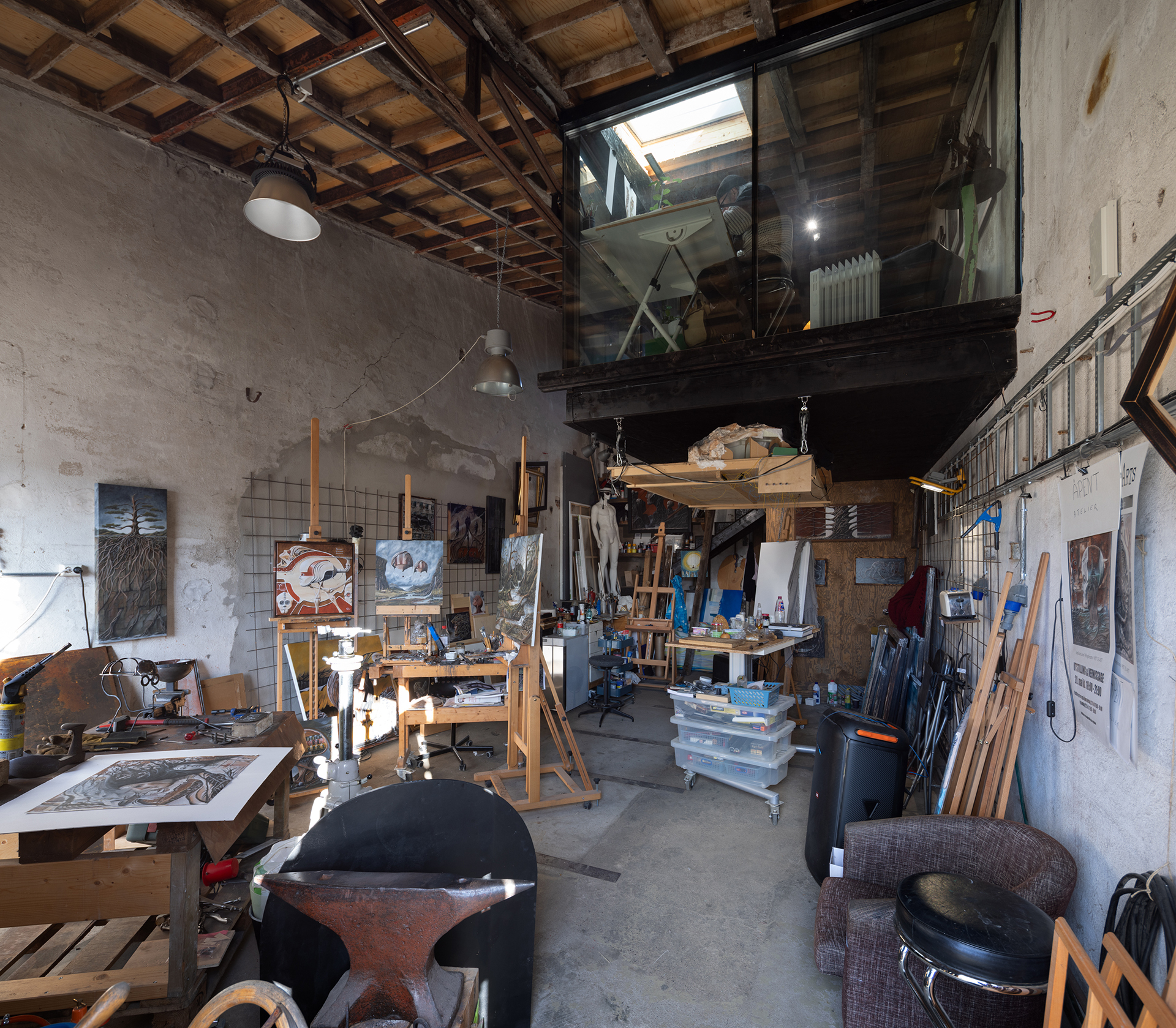 Sirkulærøkonomi i praksis 7 Kunstneratelier med staffelier, malerier, kunstartikler og diverse verktøy spredt rundt i et romslig, høyt rom med takvindu over.