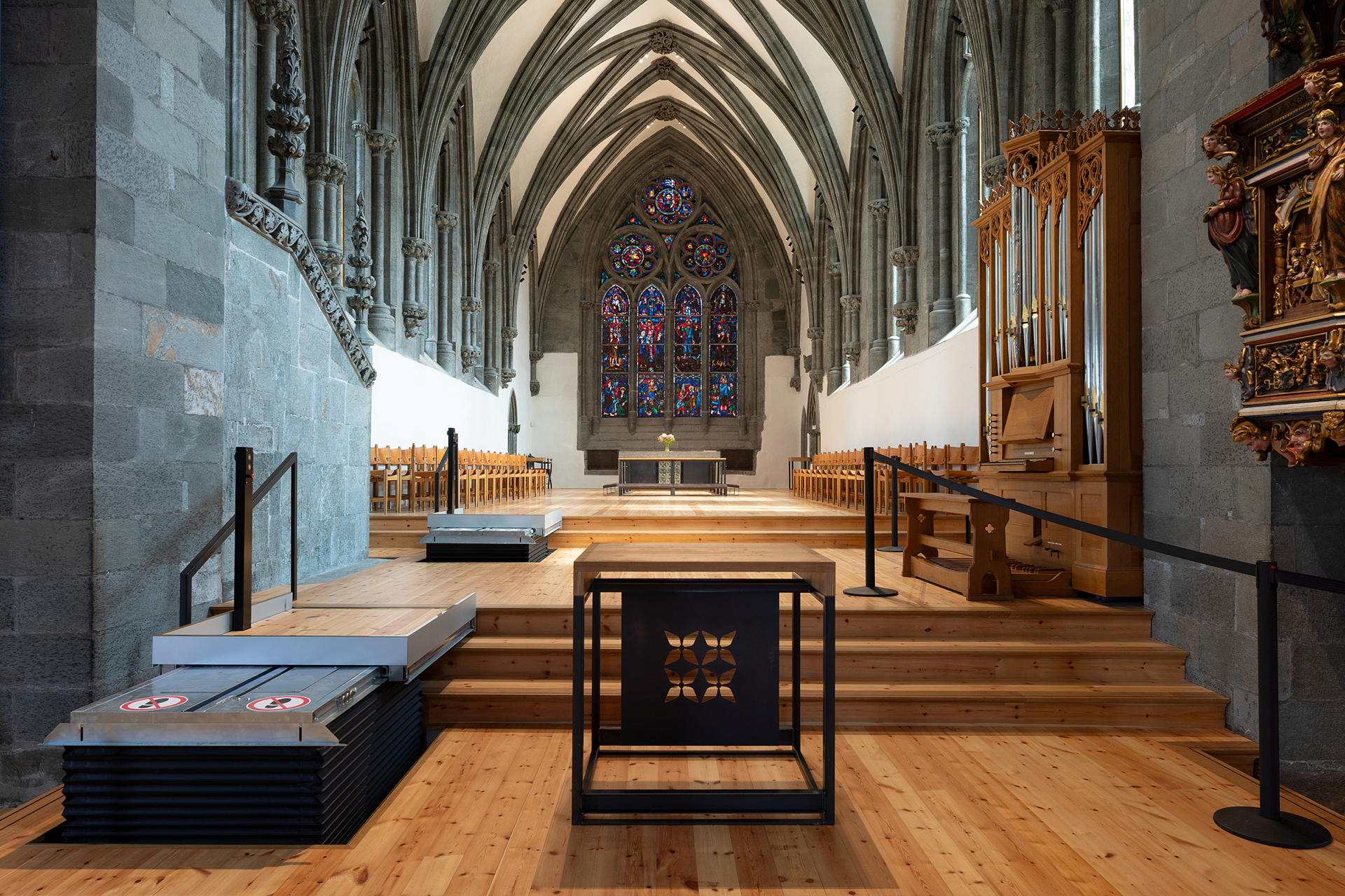 Moderne tilgjengelegheit i mellomalderkyrkje 16 Interiørbilde av en katedral i gotisk stil med hvelvede tak, glassmalerier, trebenker, et orgel og tilgjengelige plattformer i forgrunnen.