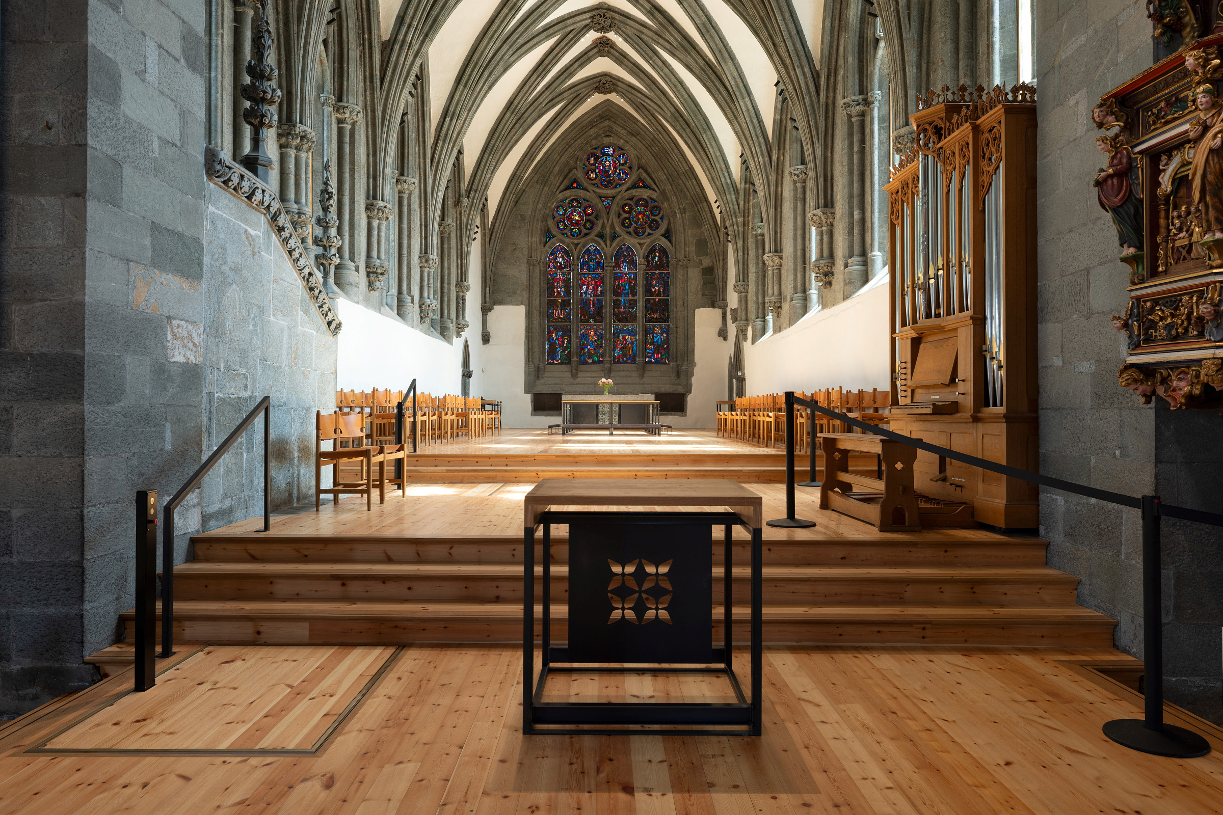 Moderne tilgjengelegheit i mellomalderkyrkje 17 Interiør i en gotisk steinkirke med hvelvede tak, glassmalerier, trebenker, orgel og et sentralt alter på en hevet plattform.