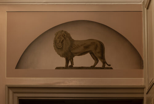 Kongegården er igjen ein konge verdig 1 Et sepiatonet veggmaleri av en løve som står på en stein, innrammet i en bueform over en døråpning innendørs.