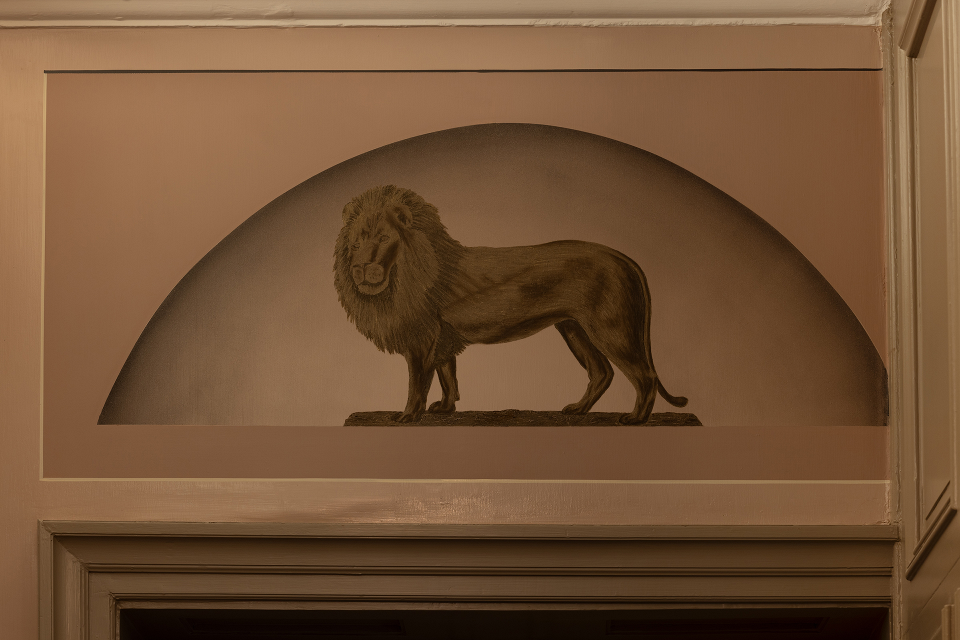 Et sepiatonet veggmaleri av en løve som står på en stein, innrammet i en bueform over en døråpning innendørs.