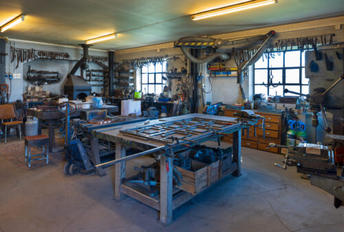 Et godt opplyst verksted med arbeidsbenker, metallverktøy, hyller og utstyr organisert langs vegger og vinduer.