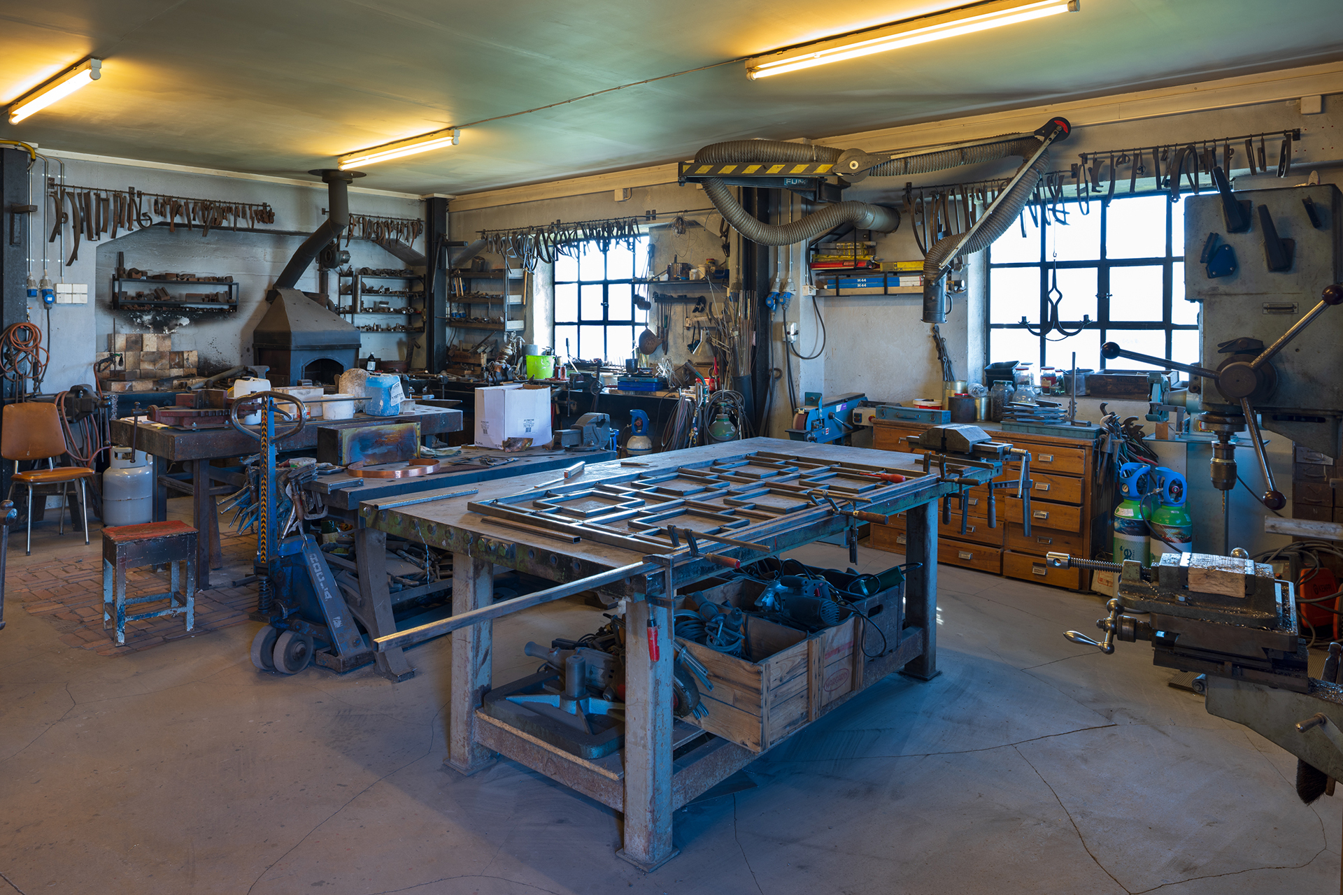 Et godt opplyst verksted med arbeidsbenker, metallverktøy, hyller og utstyr organisert langs vegger og vinduer.