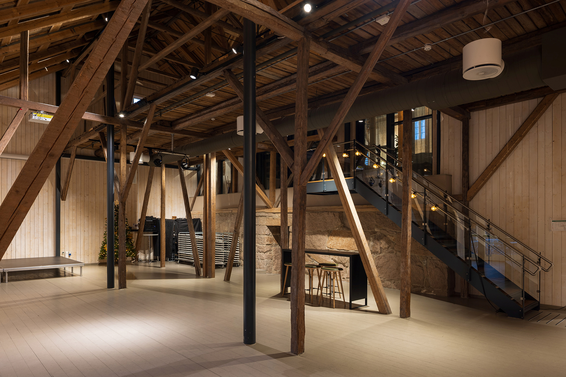 Ikkje lenger høyloft, men framleis høgt under taket 8 Romslig interiør i en renovert låve med synlige trebjelker, moderne metalltrapp, tregulv og varm belysning.