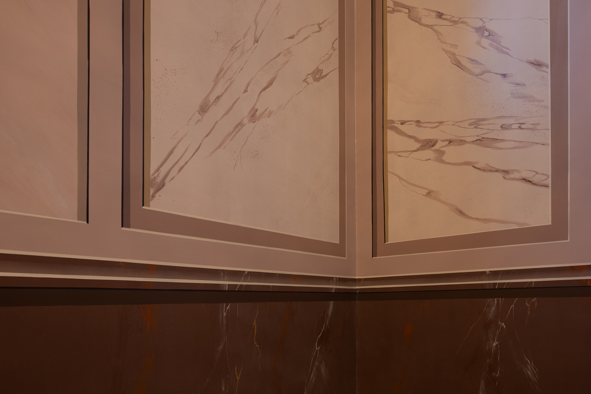 Hjørne av et rom med beige og brunt marmormønstrede veggpaneler og en mørkere nedre list, med subtile ådringer og rene linjer.