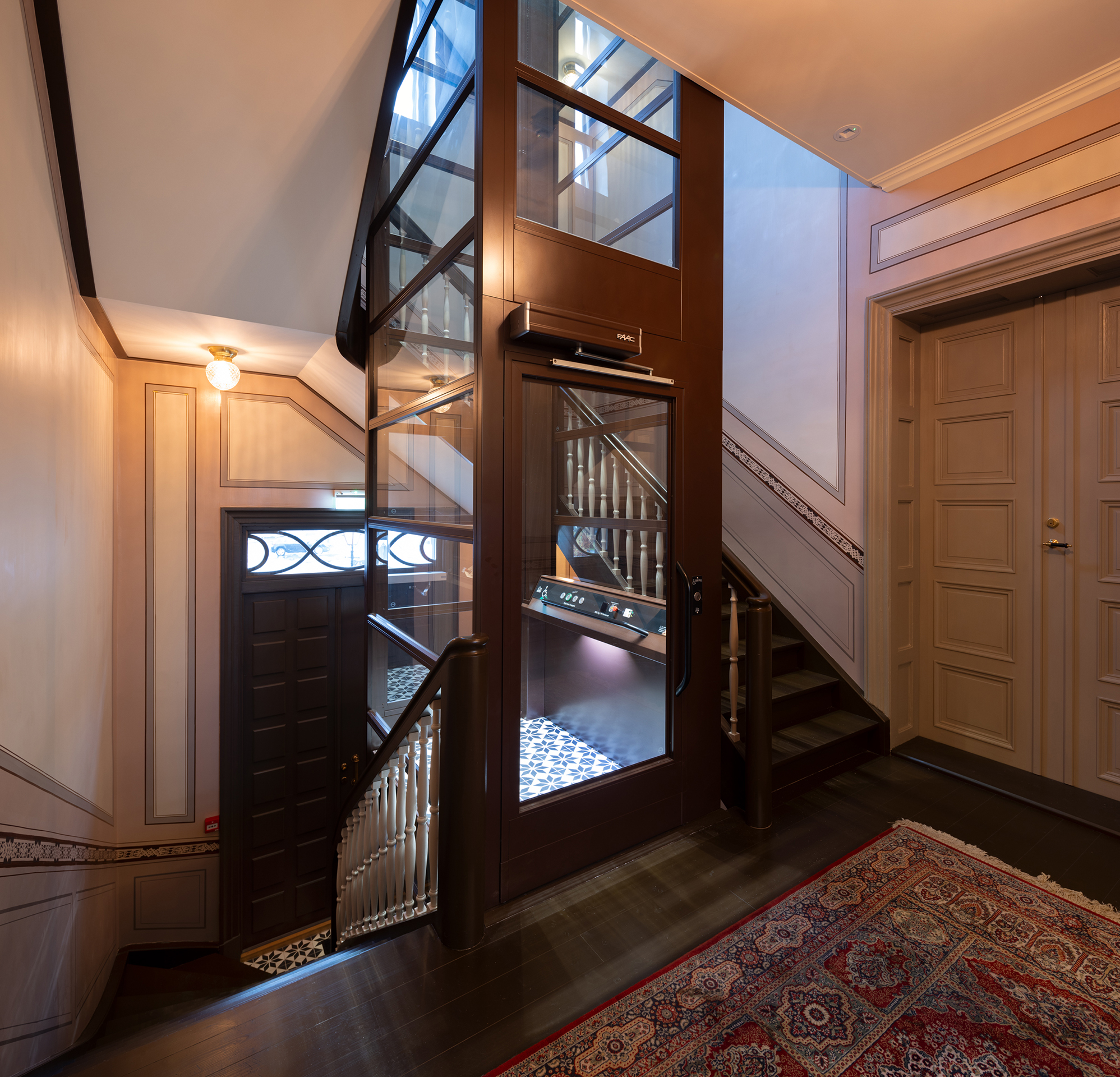 En moderne glassheis er installert i midten av et tradisjonelt trapperom med tretrinn og utsmykkede rekkverk.
