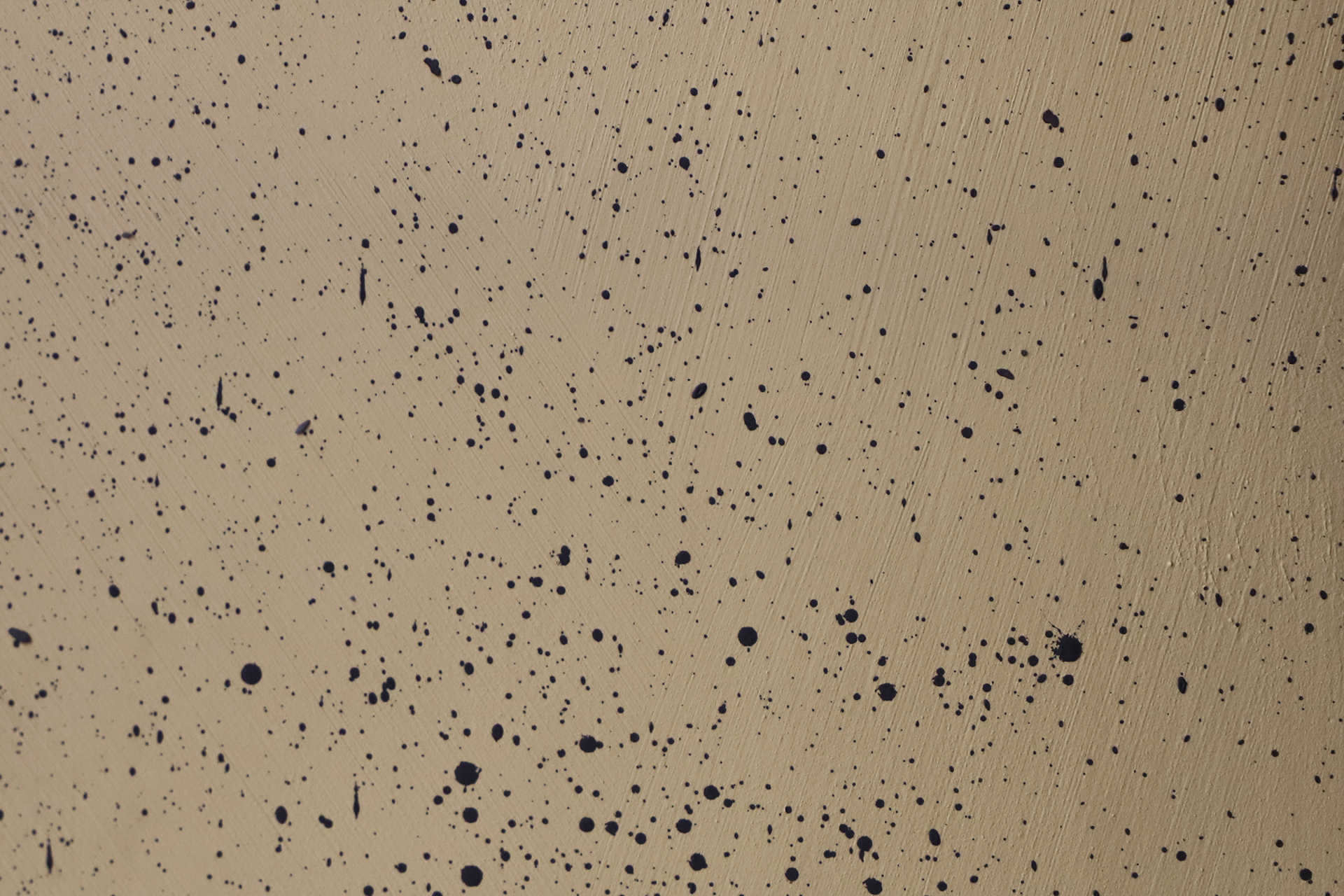 Beige overflate med spredte svarte malingsflekker og synlig penselstrøkstruktur.