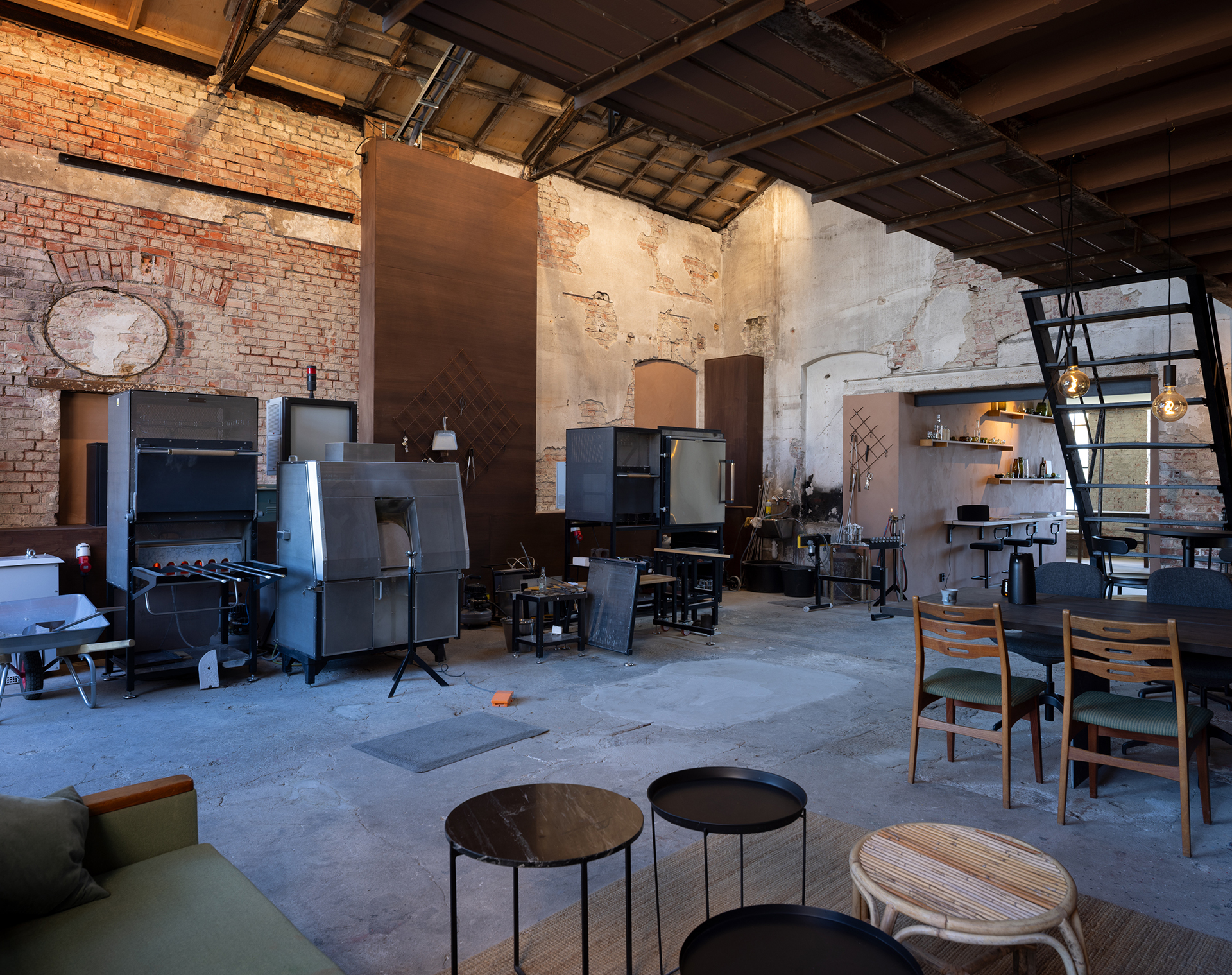 Sirkulærøkonomi i praksis 9 Romslig rom i industriell stil med synlige murvegger, diverse møbler, hyller og store metallapparater under et høyt, delvis åpent tak.