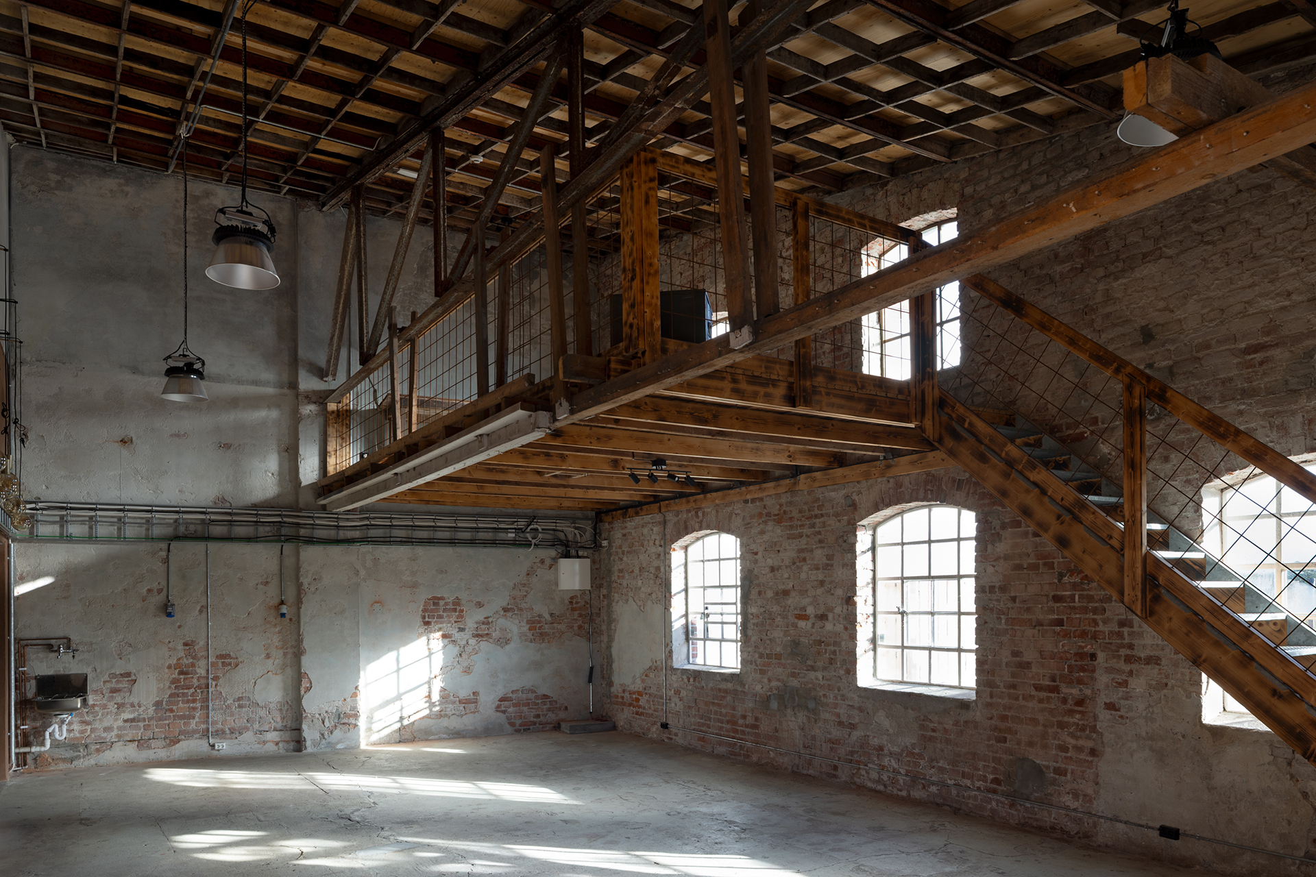 Sirkulærøkonomi i praksis 13 Interiøret i et industrielt innredet lokale med synlige murvegger, store vinduer, trebjelker, en mesanin og en trapp som leder opp til denne.