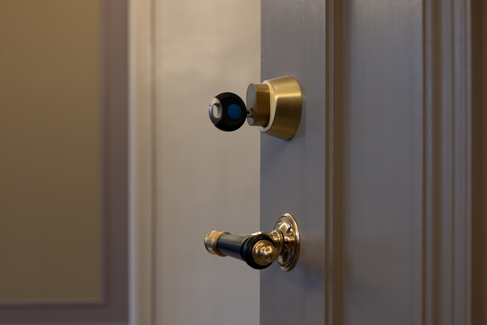 Nærbilde av en delvis åpen dør med et moderne dørhåndtak i messing og en svart smartlås montert over.