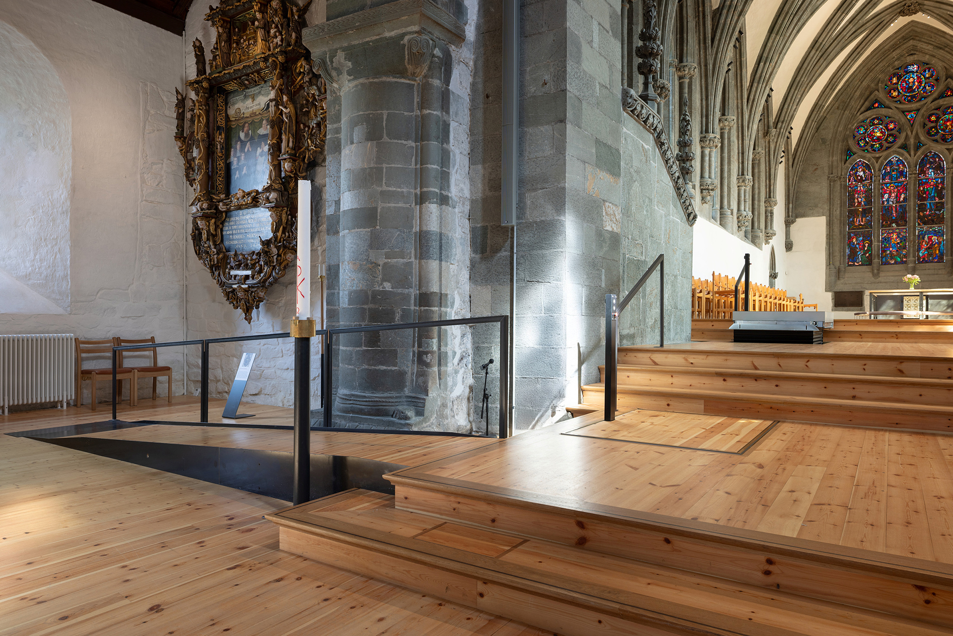Moderne tilgjengelegheit i mellomalderkyrkje 13 Moderne trerampe og trapper gir tilgjengelig inngang i en historisk steinkirke med hvelvede tak og glassmalerier.