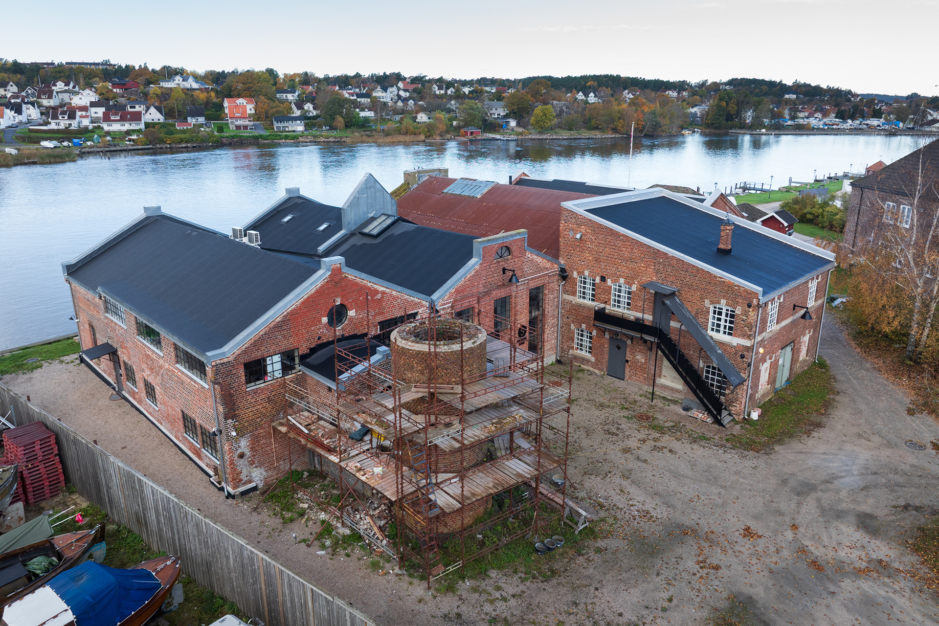Sirkulærøkonomi i praksis 16 Flyfoto av en industribygning i murstein som er under delvis renovering, med stillas rundt en rund bygning, ved siden av en elv og et boligområde i bakgrunnen.