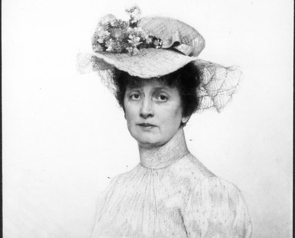 Svart-hvitt portrett av en kvinne iført høyhalset kjole og stor hatt med blomster og blonder, som ser direkte inn i kameraet.