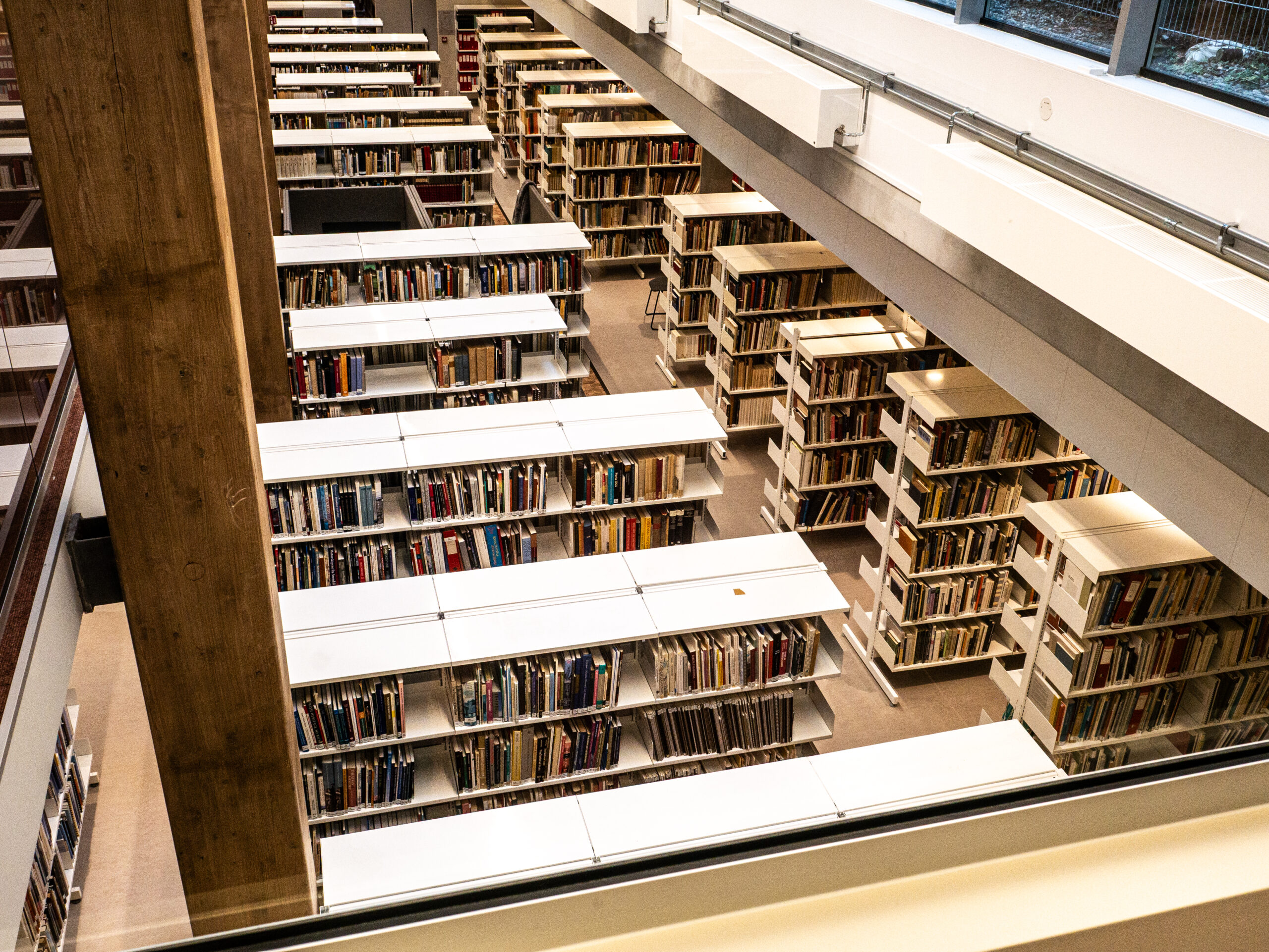 Rader av bokhyller fylt med bøker er sirlig plassert i et stort, moderne bibliotek sett fra en av de øverste etasjene.