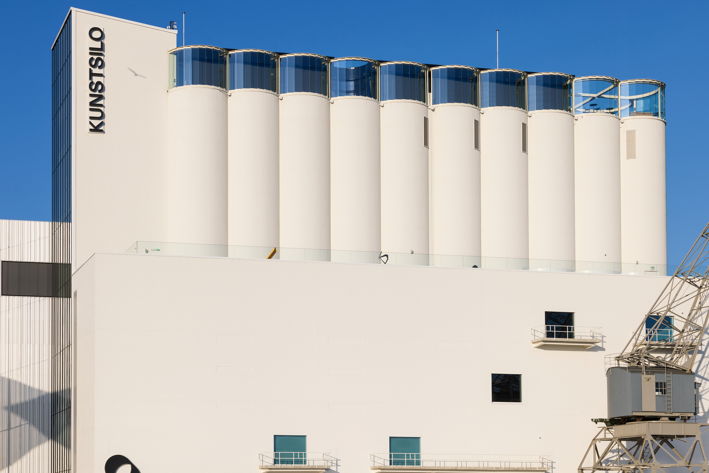 En moderne hvit bygning med høye sylinderformede siloer og KUNSTSILO skrevet vertikalt på siden, mot en klar blå himmel.